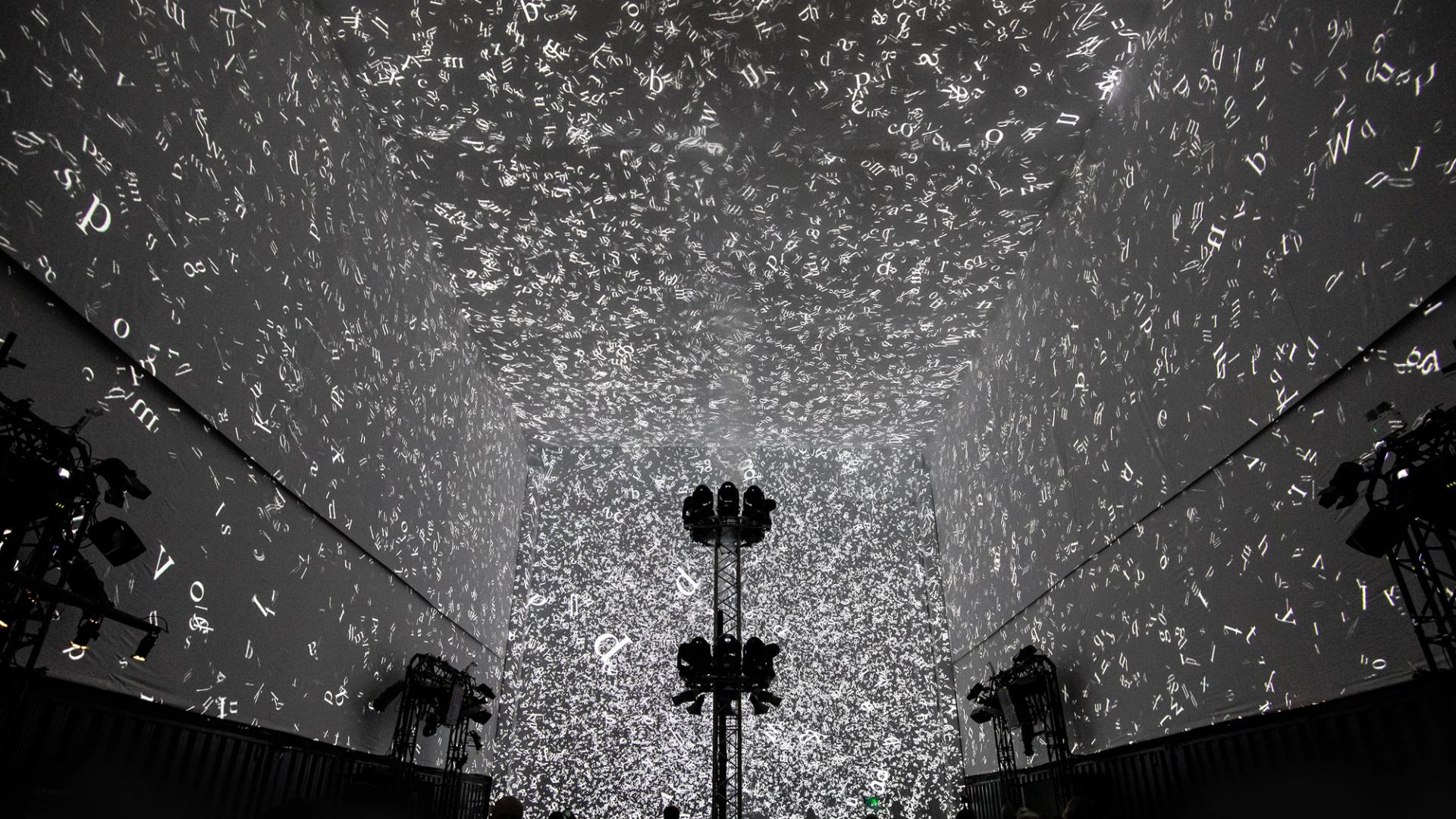 Silhouettes of 3 people walking in front of the Cloud Display, a wall of smoke simulating cloud vapour