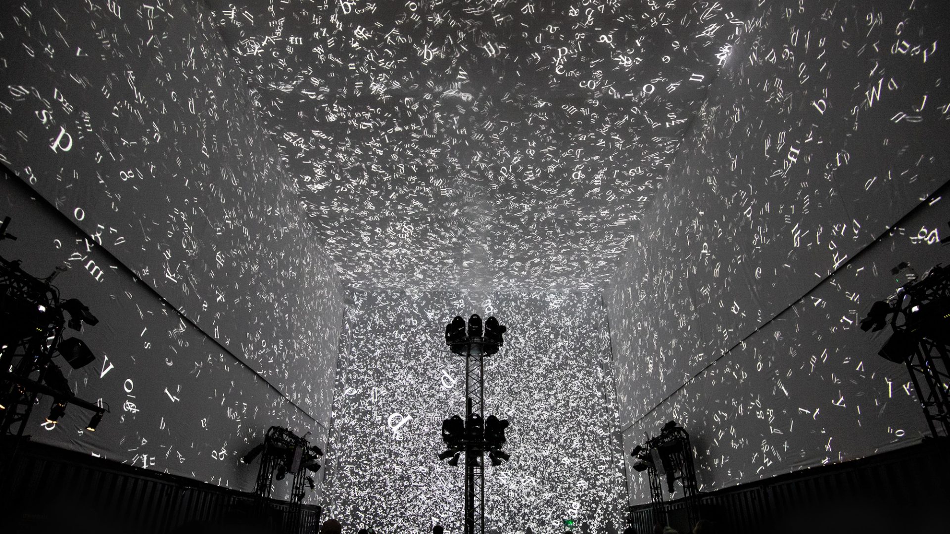 Silhouettes of 3 people walking in front of the Cloud Display, a wall of smoke simulating cloud vapour