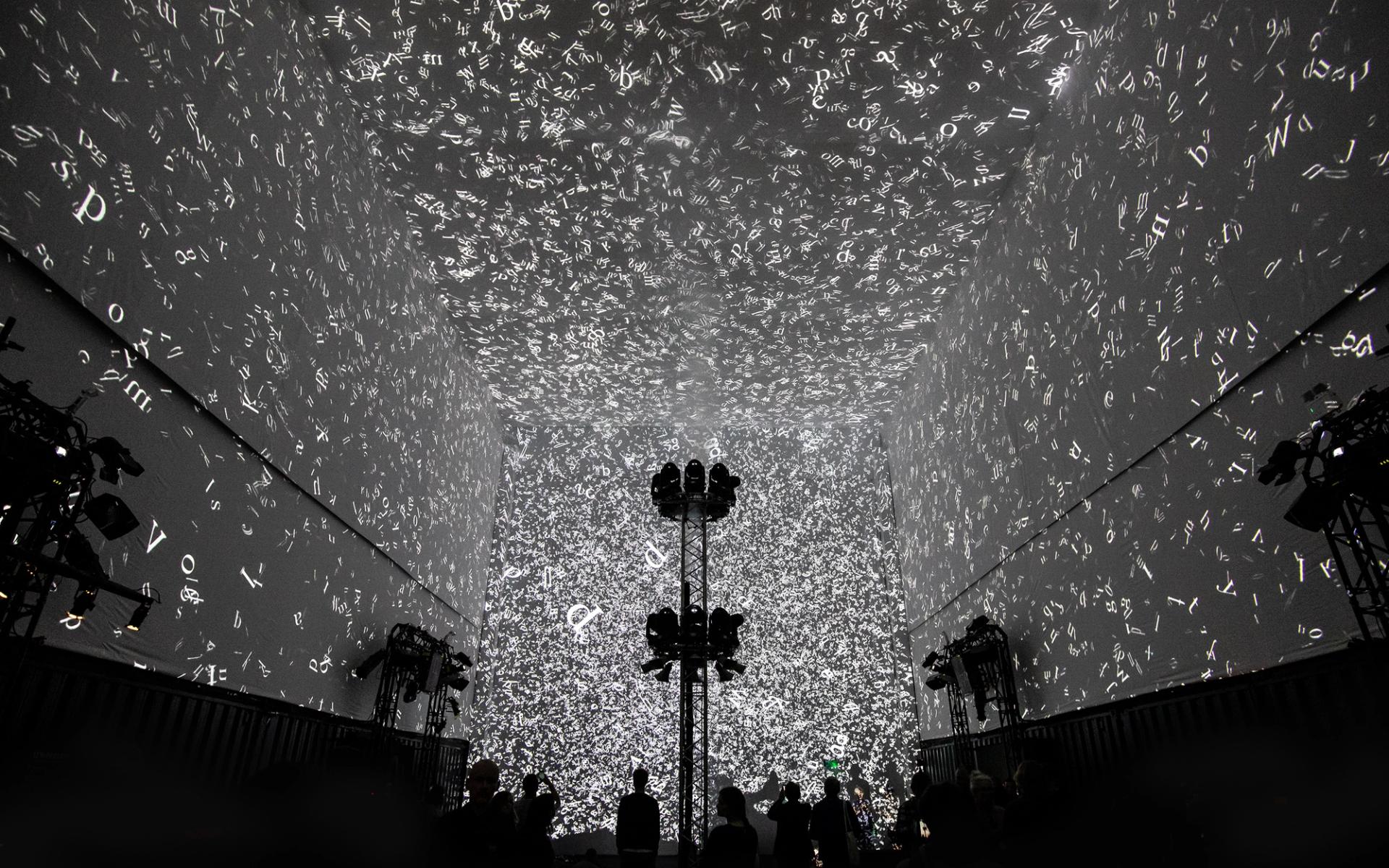 Silhouettes of 3 people walking in front of the Cloud Display, a wall of smoke simulating cloud vapour