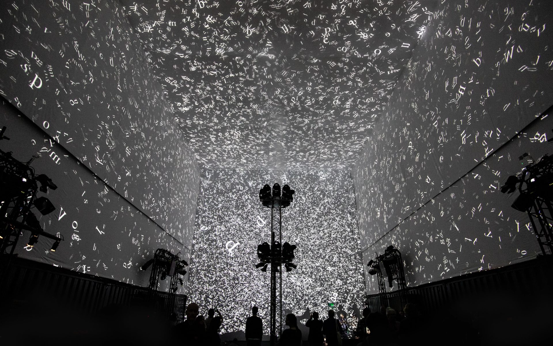 Silhouettes of 3 people walking in front of the Cloud Display, a wall of smoke simulating cloud vapour
