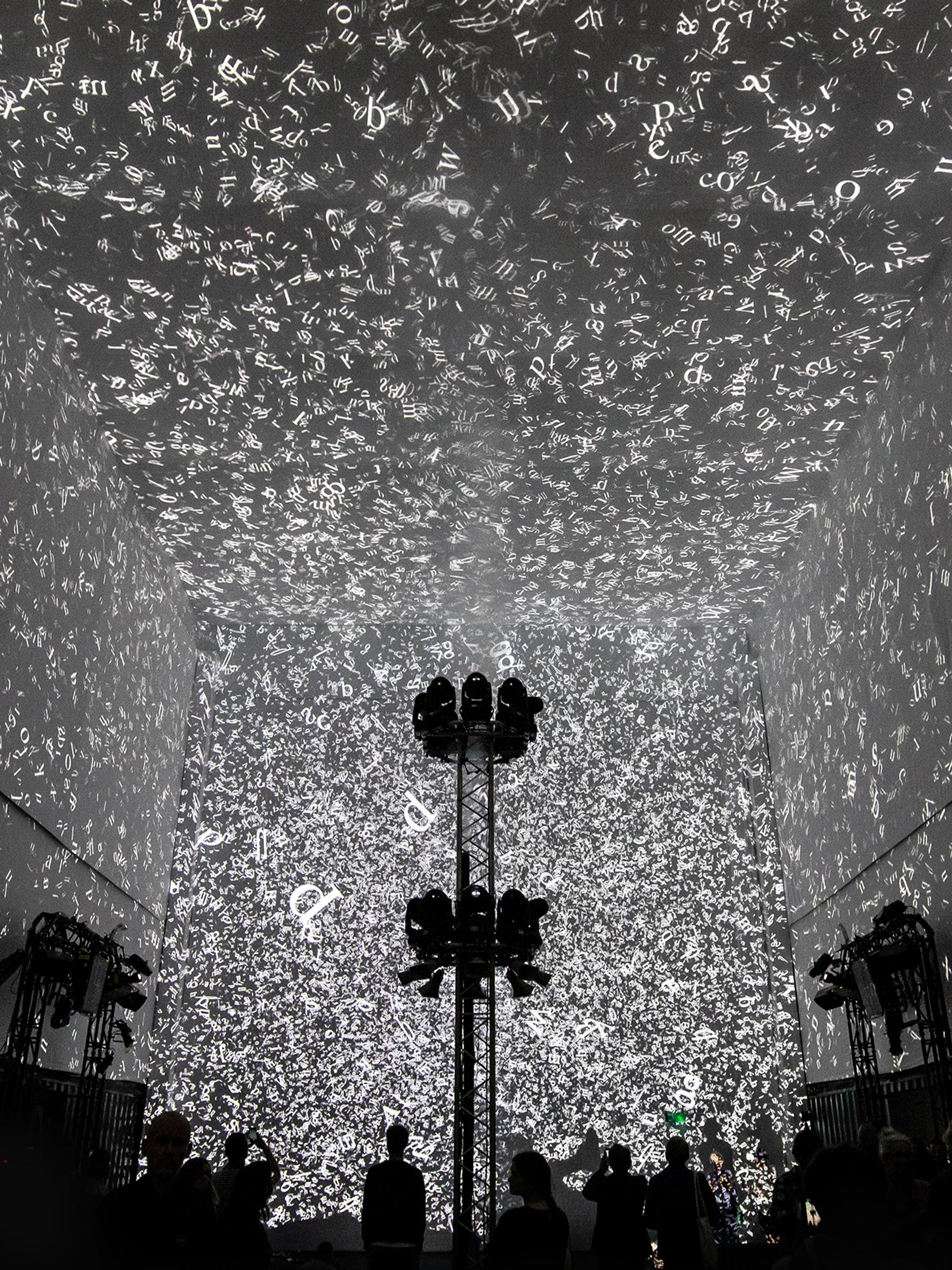 Silhouettes of 3 people walking in front of the Cloud Display, a wall of smoke simulating cloud vapour