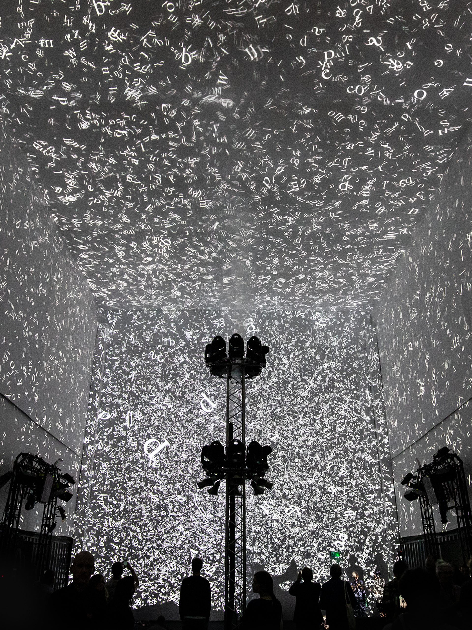 Silhouettes of 3 people walking in front of the Cloud Display, a wall of smoke simulating cloud vapour