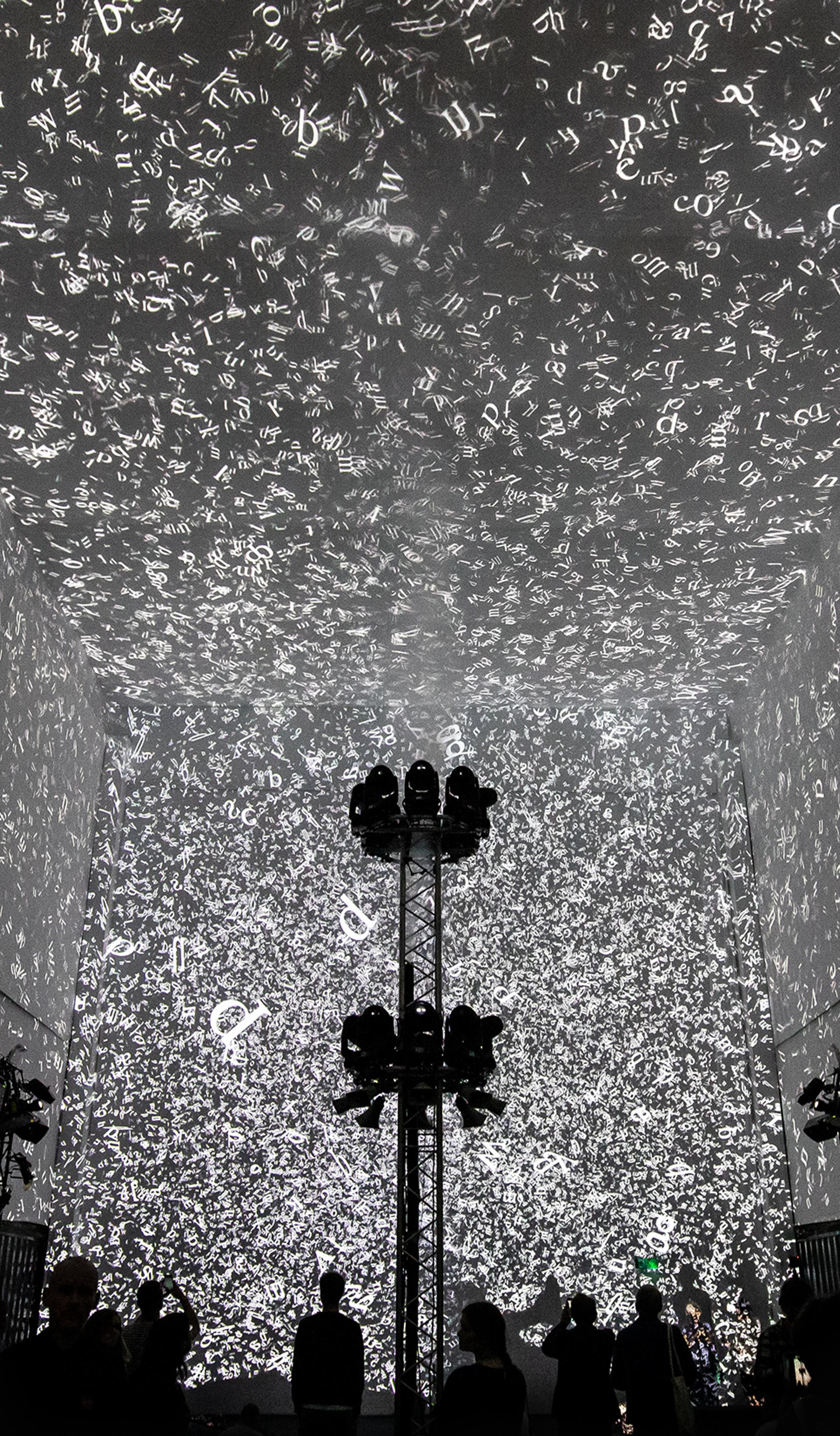 Silhouettes of 3 people walking in front of the Cloud Display, a wall of smoke simulating cloud vapour