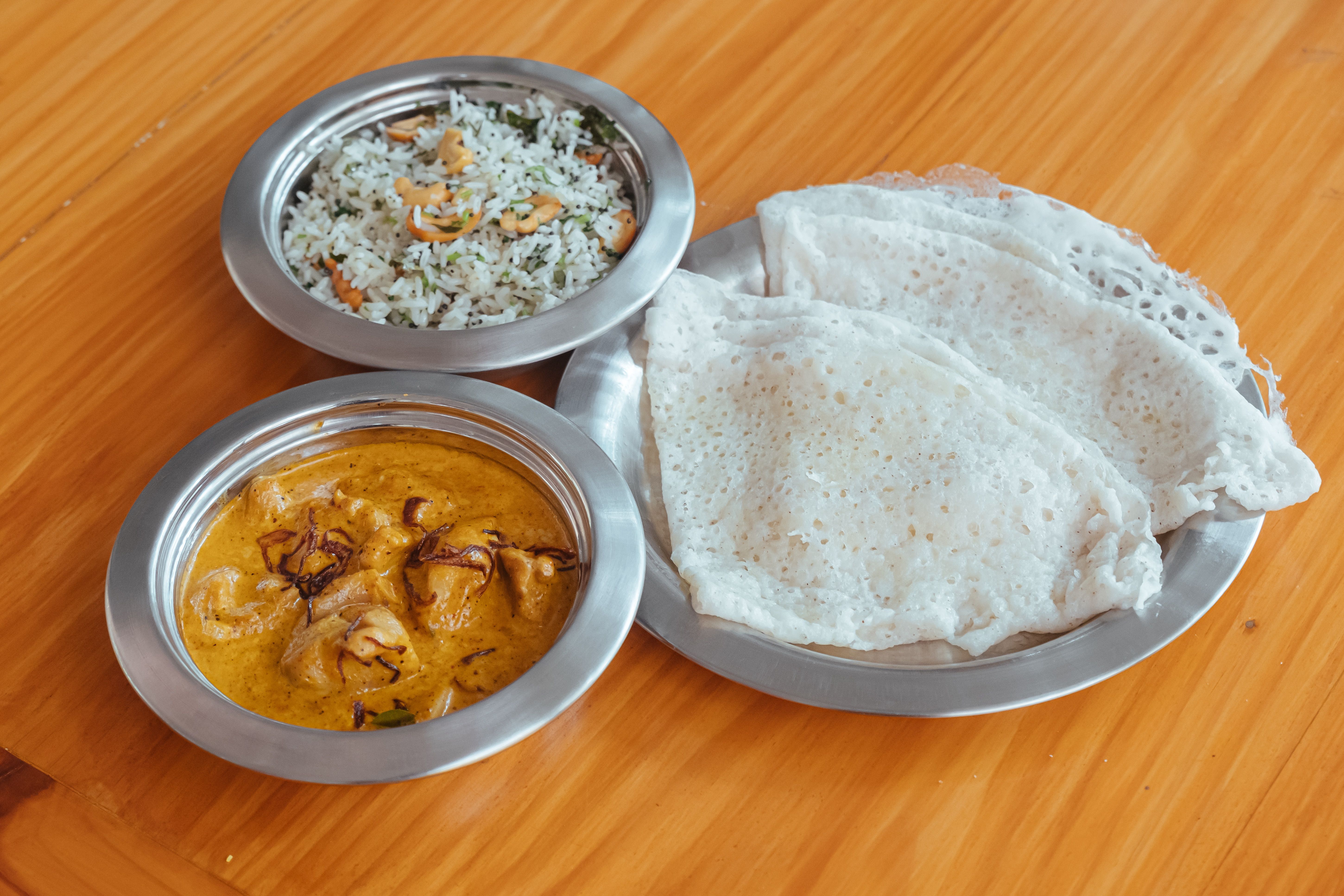 A serving of chicken curry, rice and rotti, in individual shallow silver dishes.