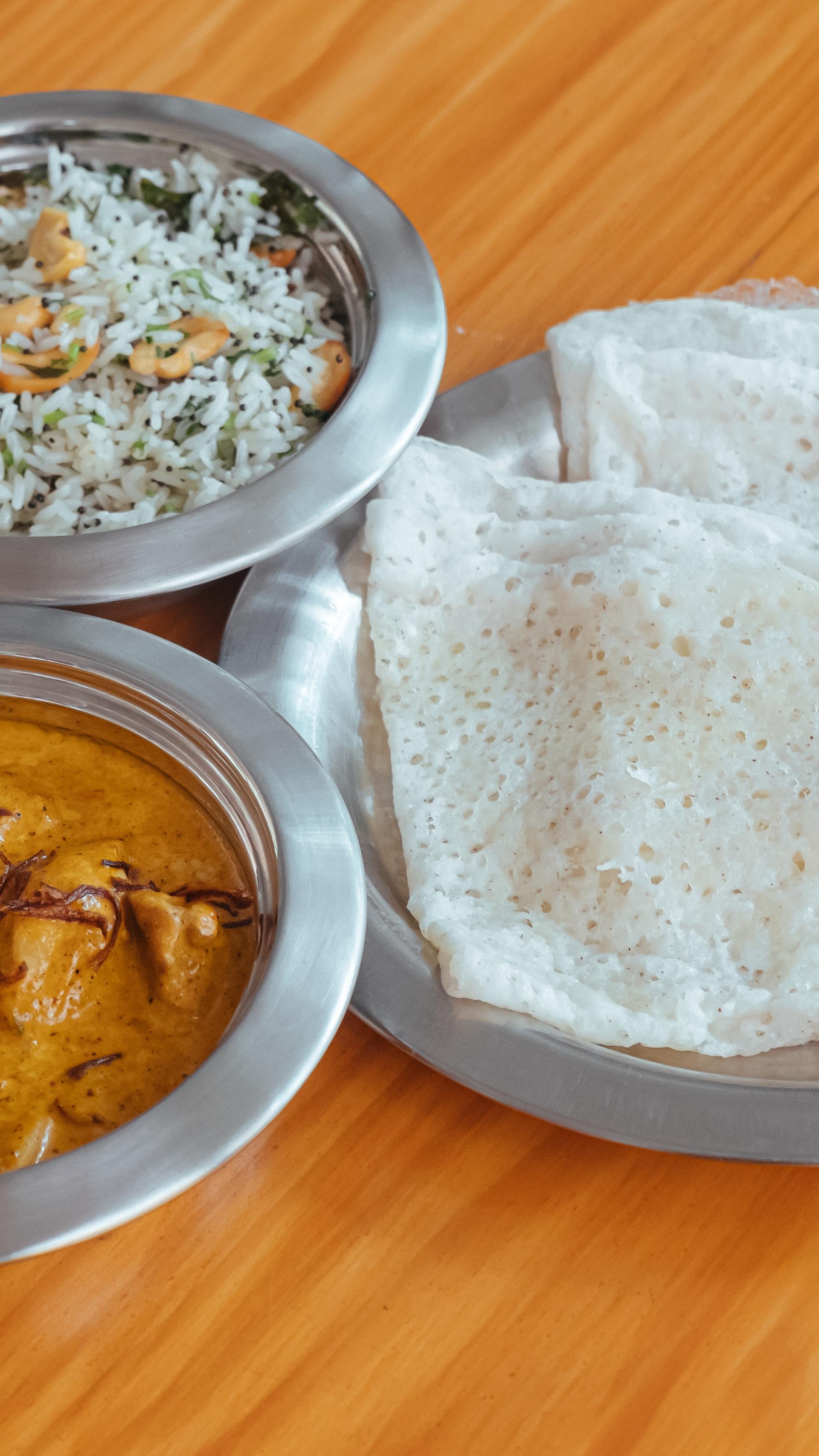 A serving of chicken curry, rice and rotti, in individual shallow silver dishes.