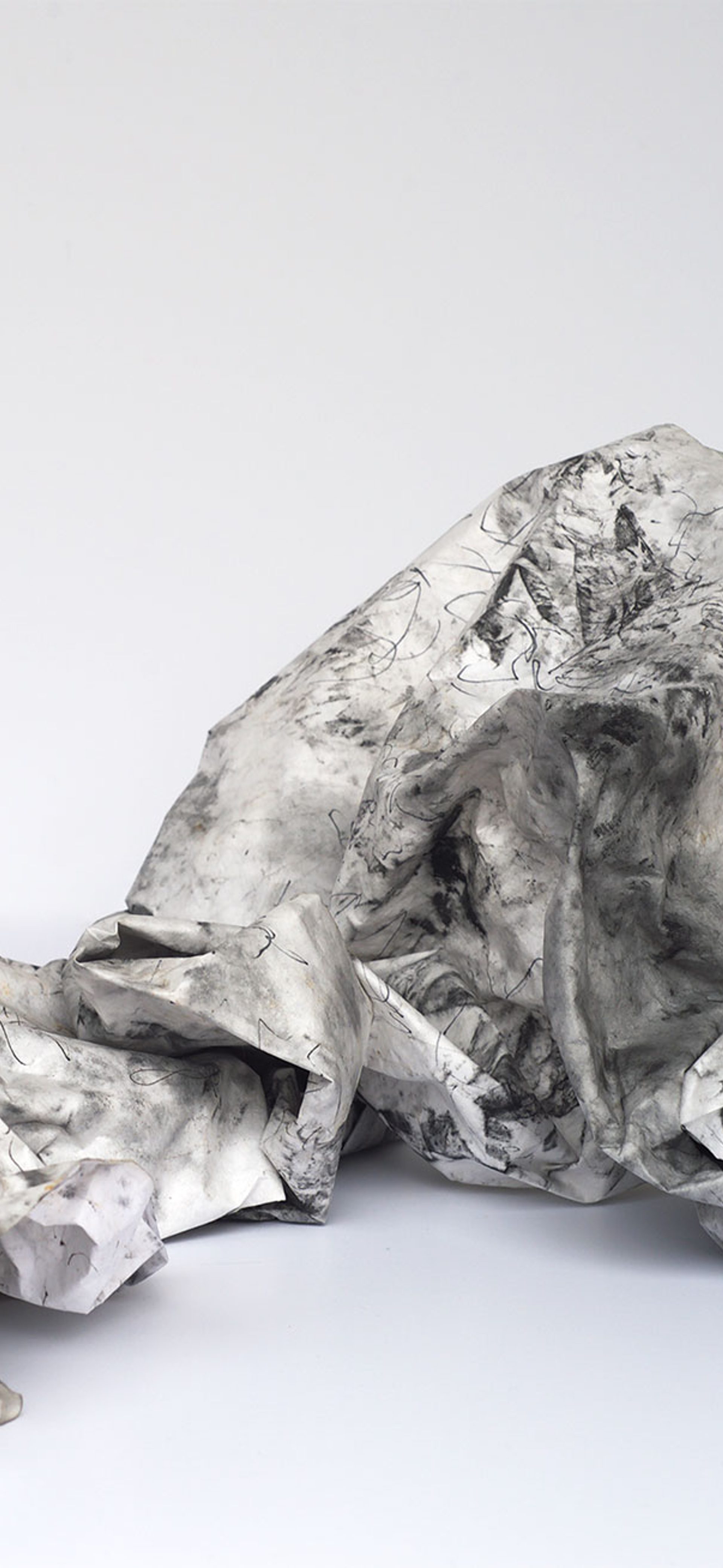 An artwork made of white paper and black ink on a grey background. The paper is crumpled and folded upon itself.