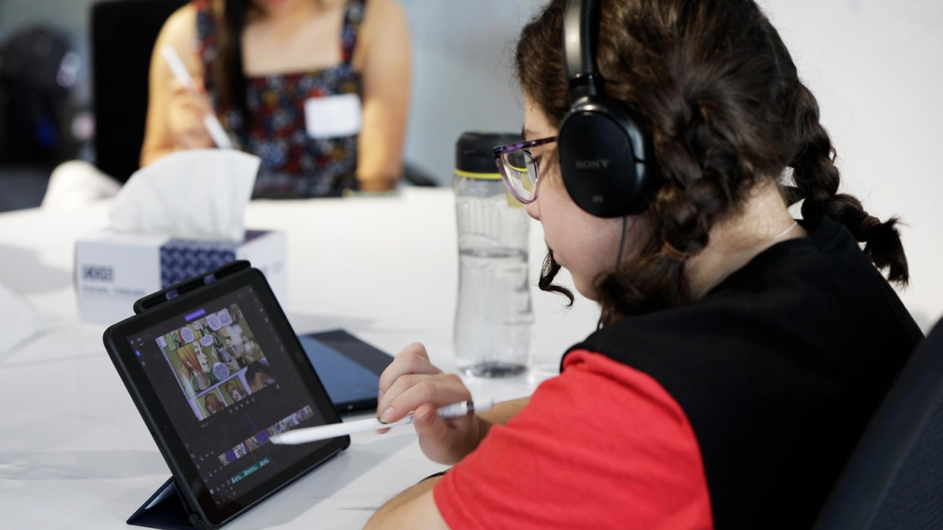 A Creative Studio participant wearing a red and black shirt and braided pigtails draws on a touch screen.