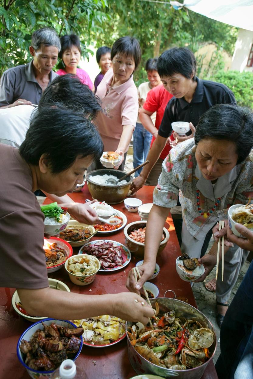 A group of people gathered around an outdoor table laden with a variety of colourful and appetising dishes.