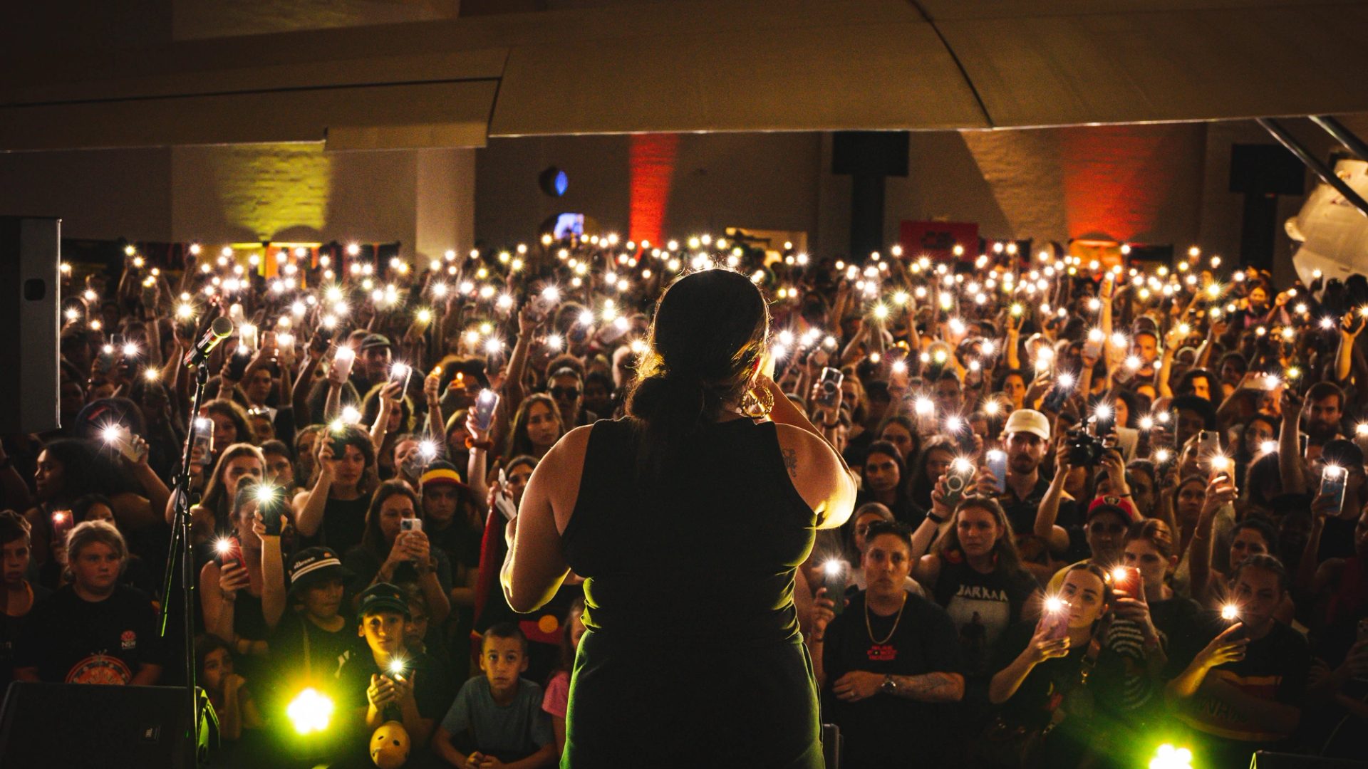 A woman performs in front of an audience who are holding their phone lights in the air.
