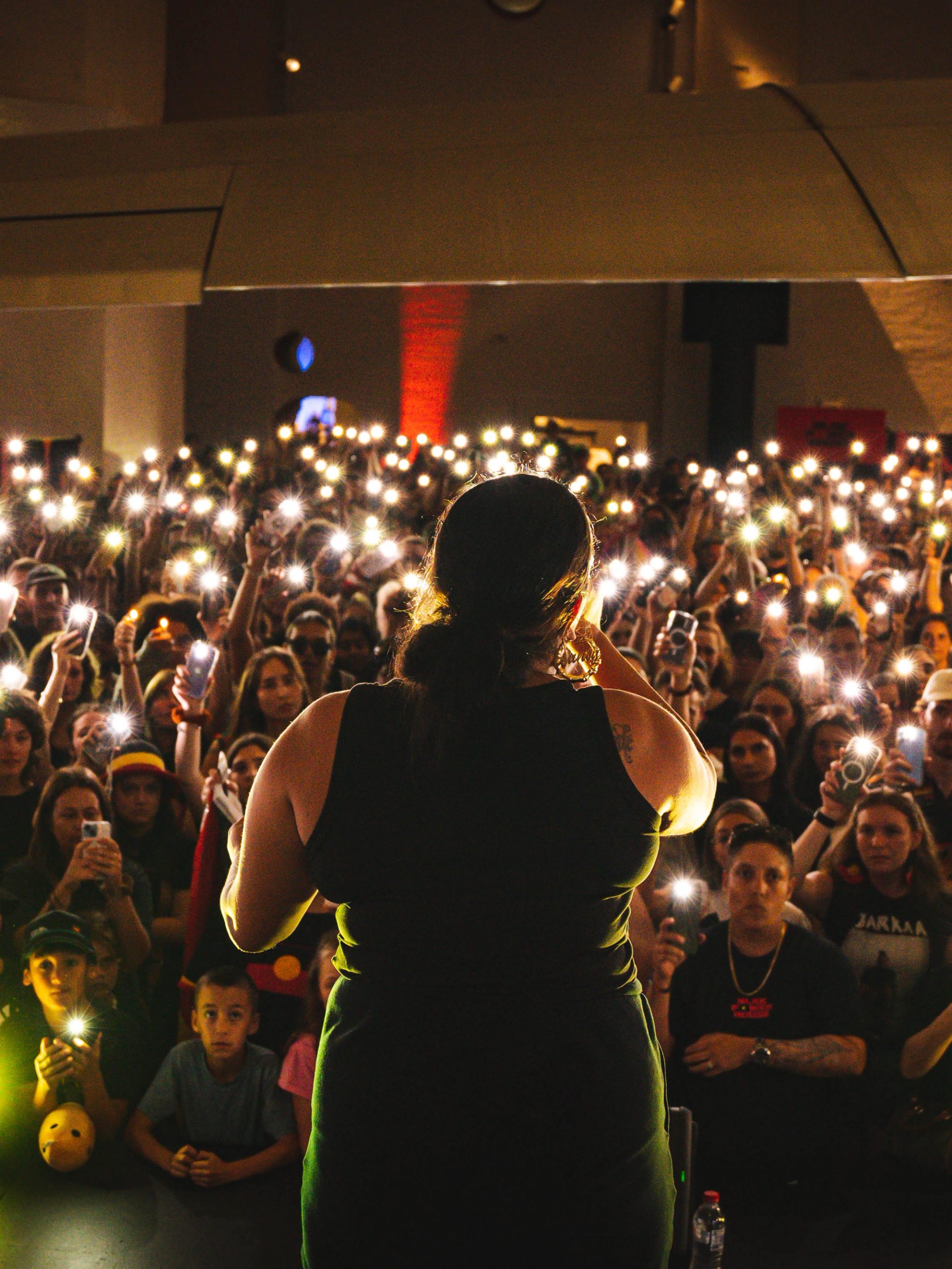A woman performs in front of an audience who are holding their phone lights in the air.