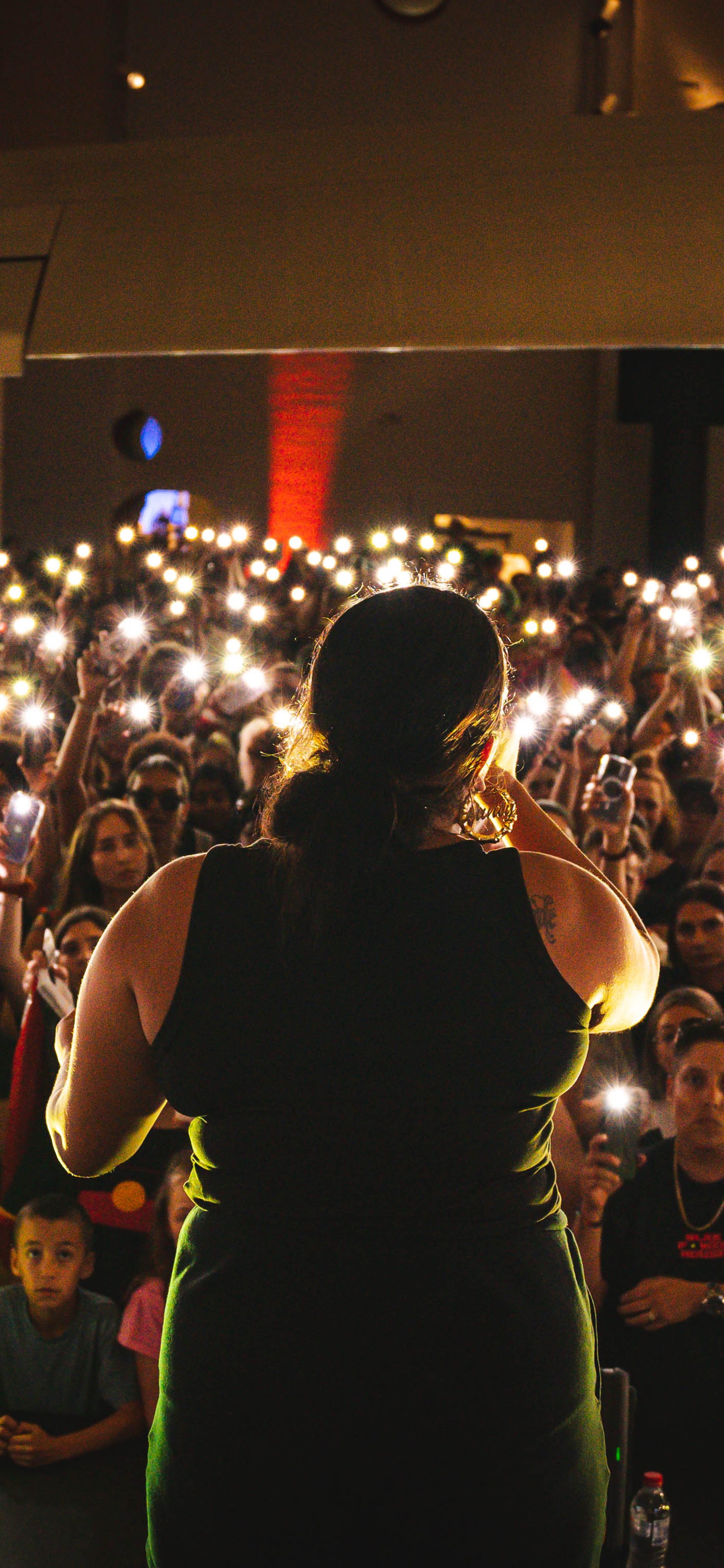 A woman performs in front of an audience who are holding their phone lights in the air.