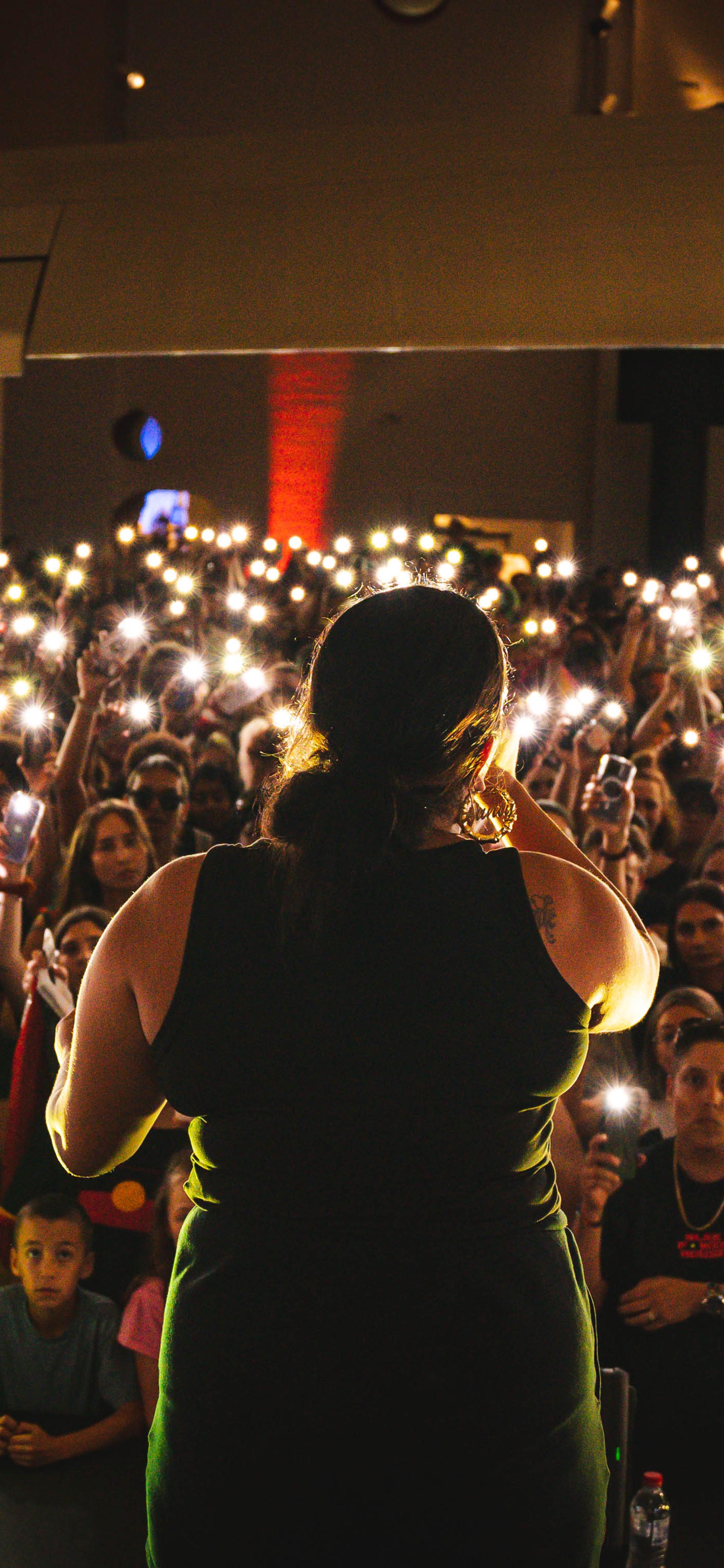 A woman performs in front of an audience who are holding their phone lights in the air.