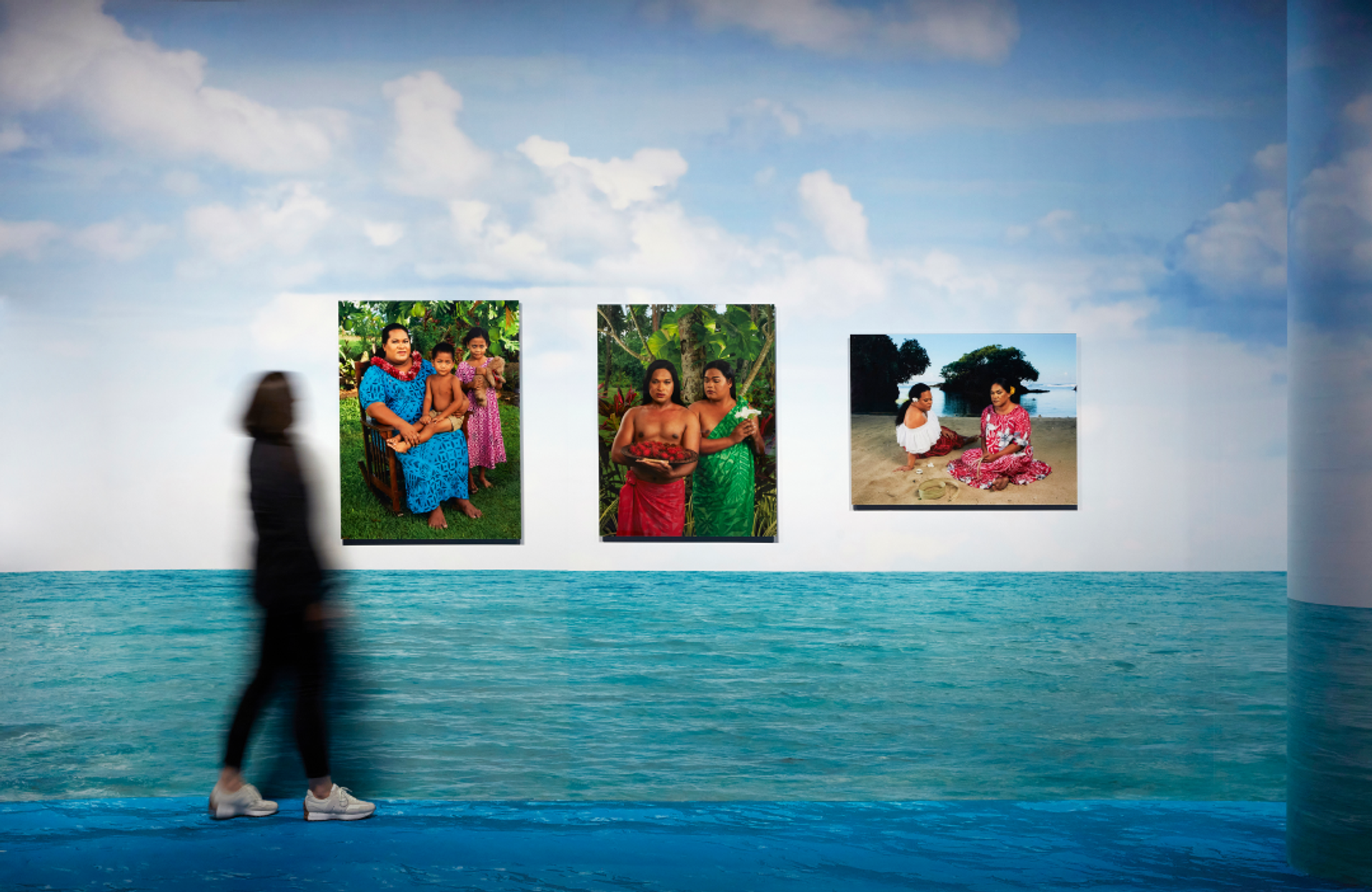 Figure walks in front of three artworks on wall that looks like the ocean