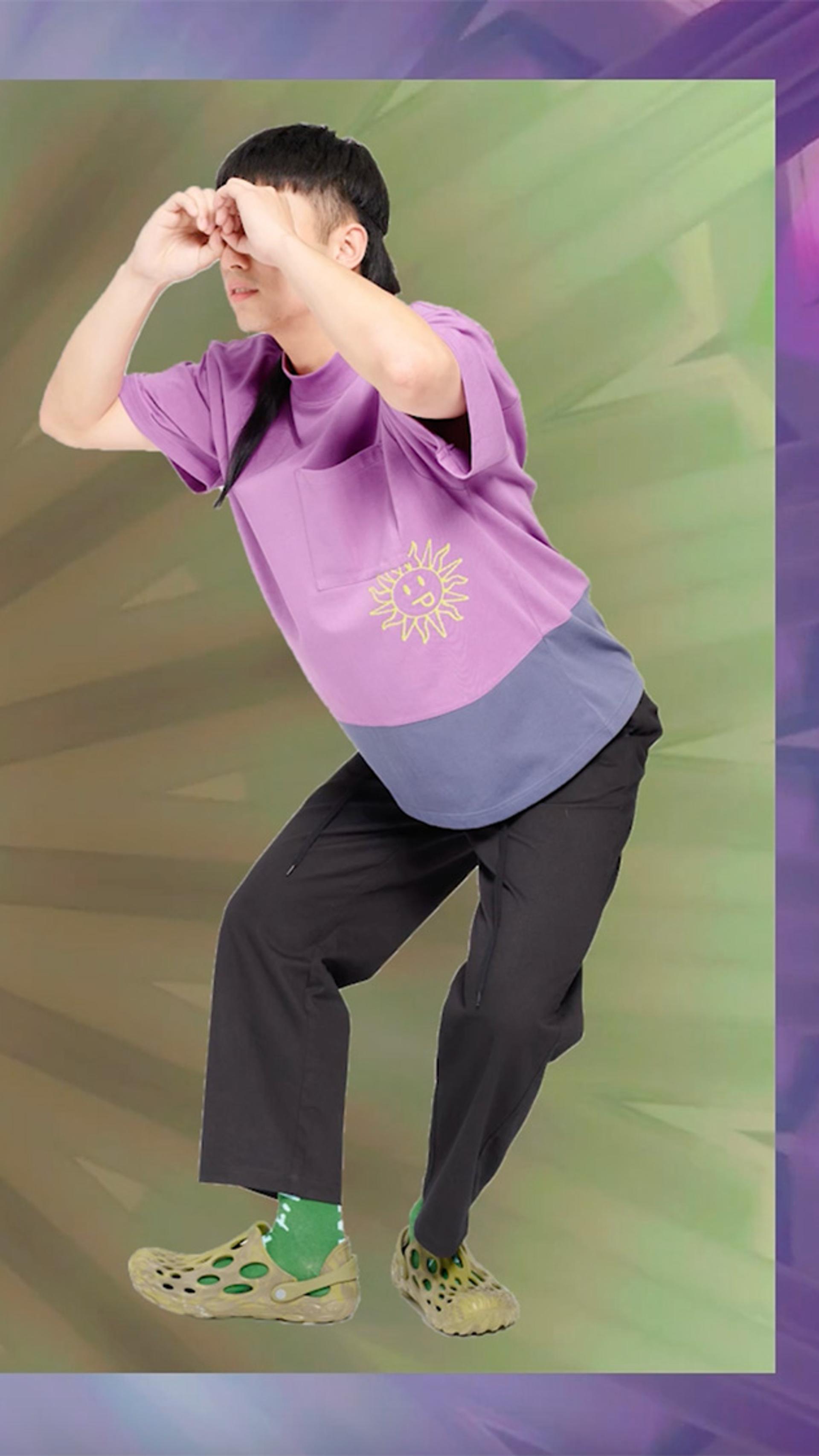 On the left hand side is a purple bike, on the right hand side is a person wearing a purple shirt, black pants and olive coloured shoes making the shape of a telescope out of their hands.