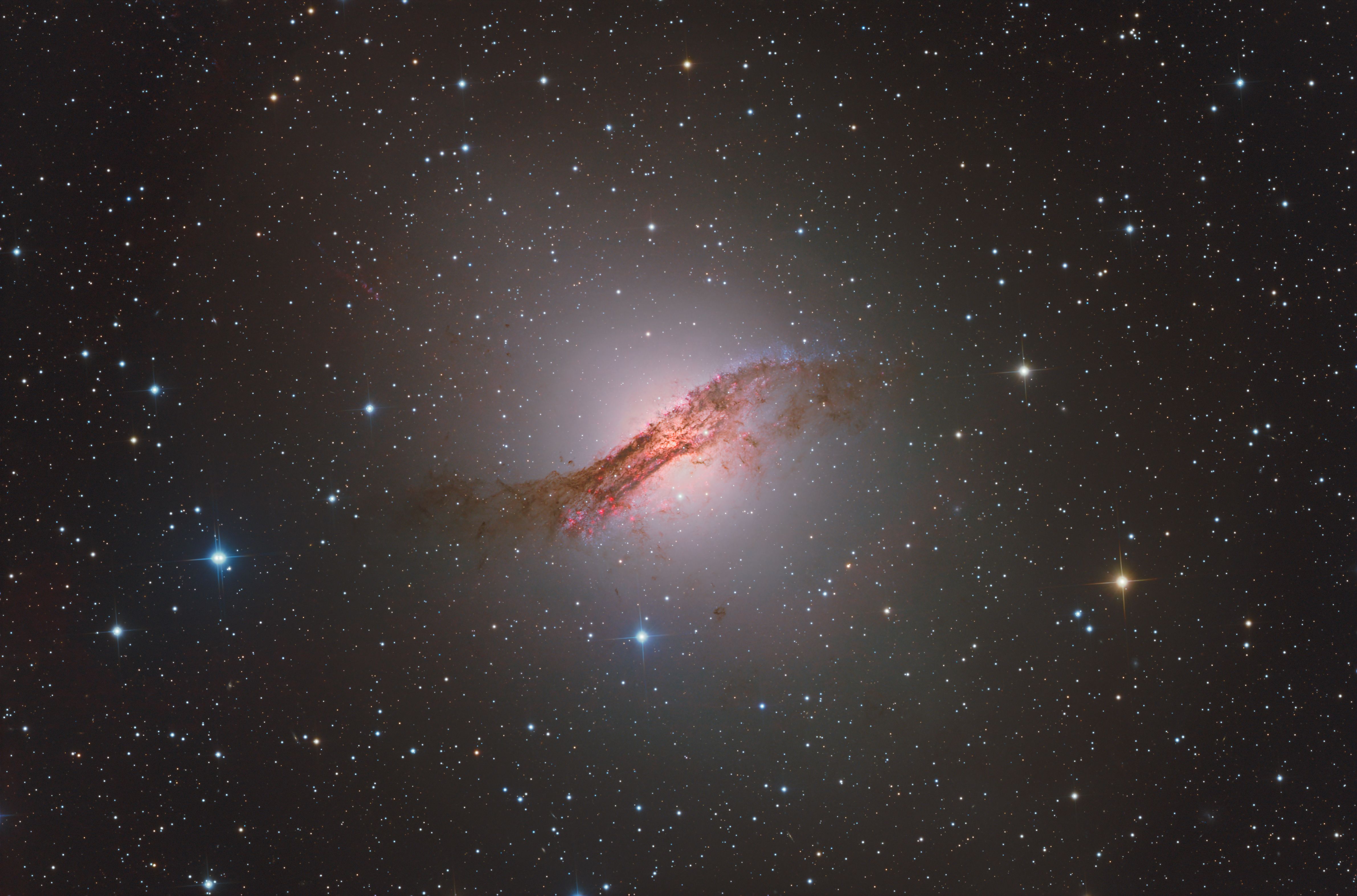 Telescopic image of the space sky featuring the constellation Centaurus, a spiral galaxy of red dust/gas with a bright light in the centre. Surrounded by an endless number of stars.