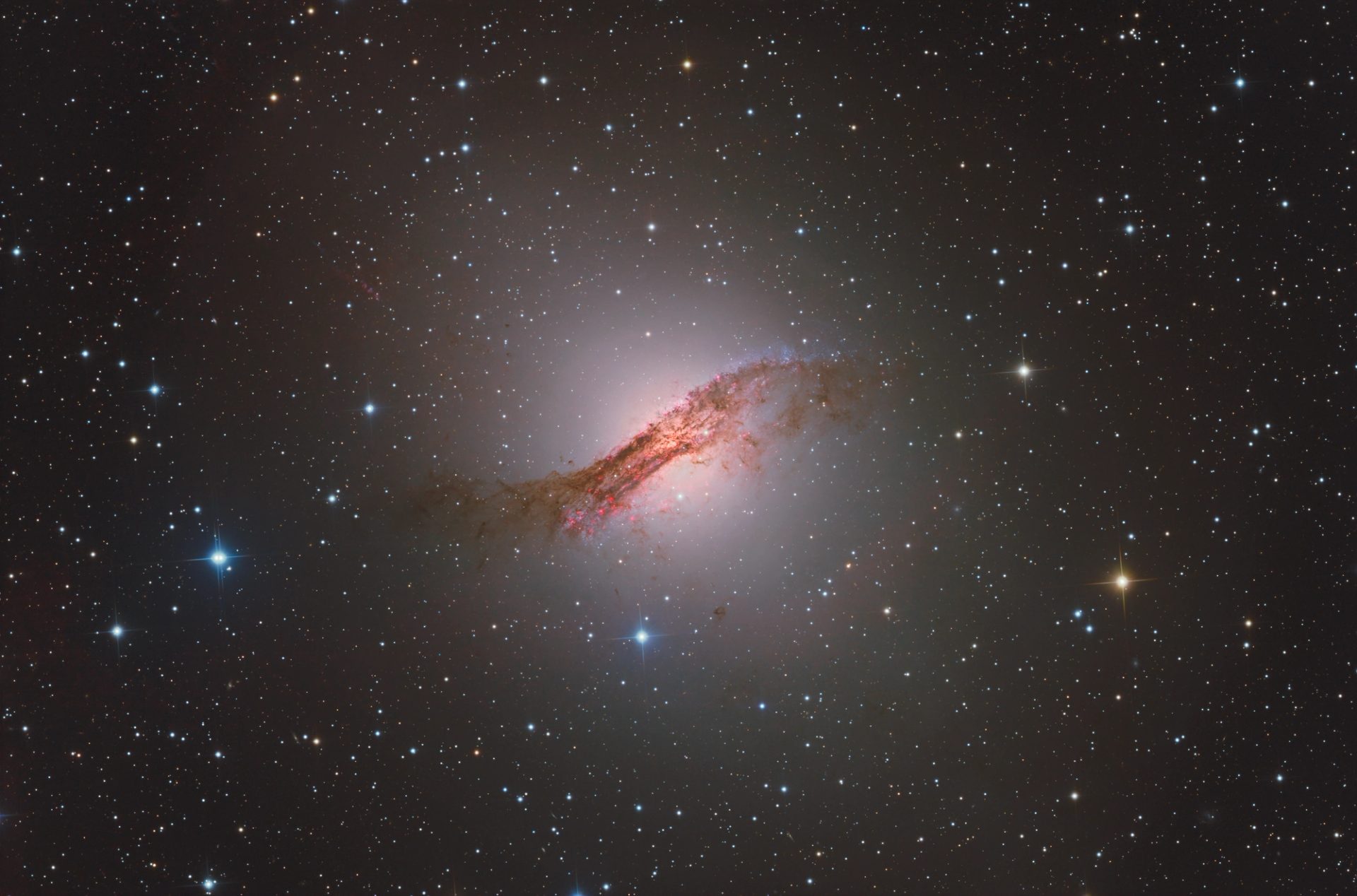 Telescopic image of the space sky featuring the constellation Centaurus, a spiral galaxy of red dust/gas with a bright light in the centre. Surrounded by an endless number of stars.