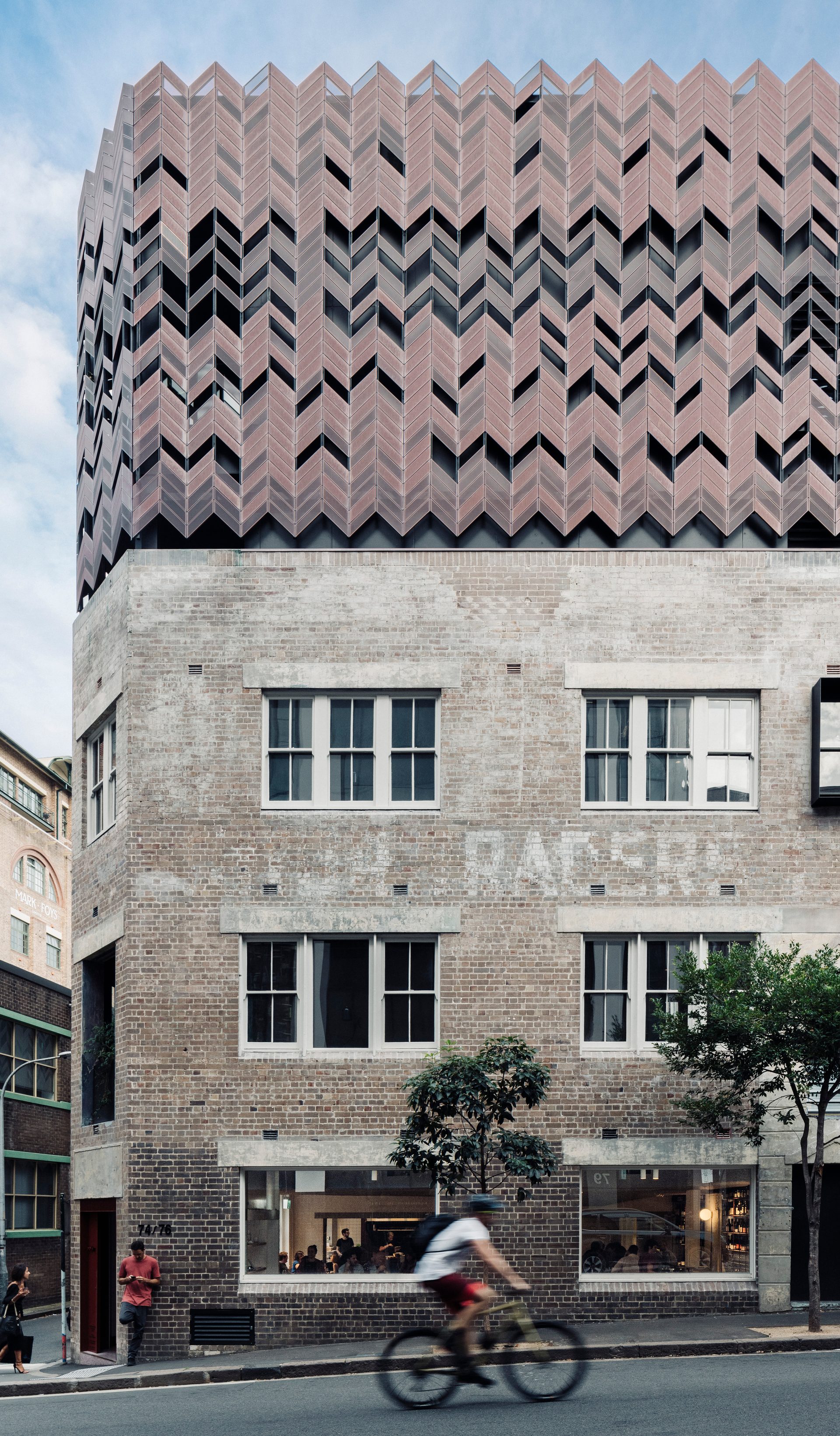 A blurry bicycle rider rides past a building in the foreground.