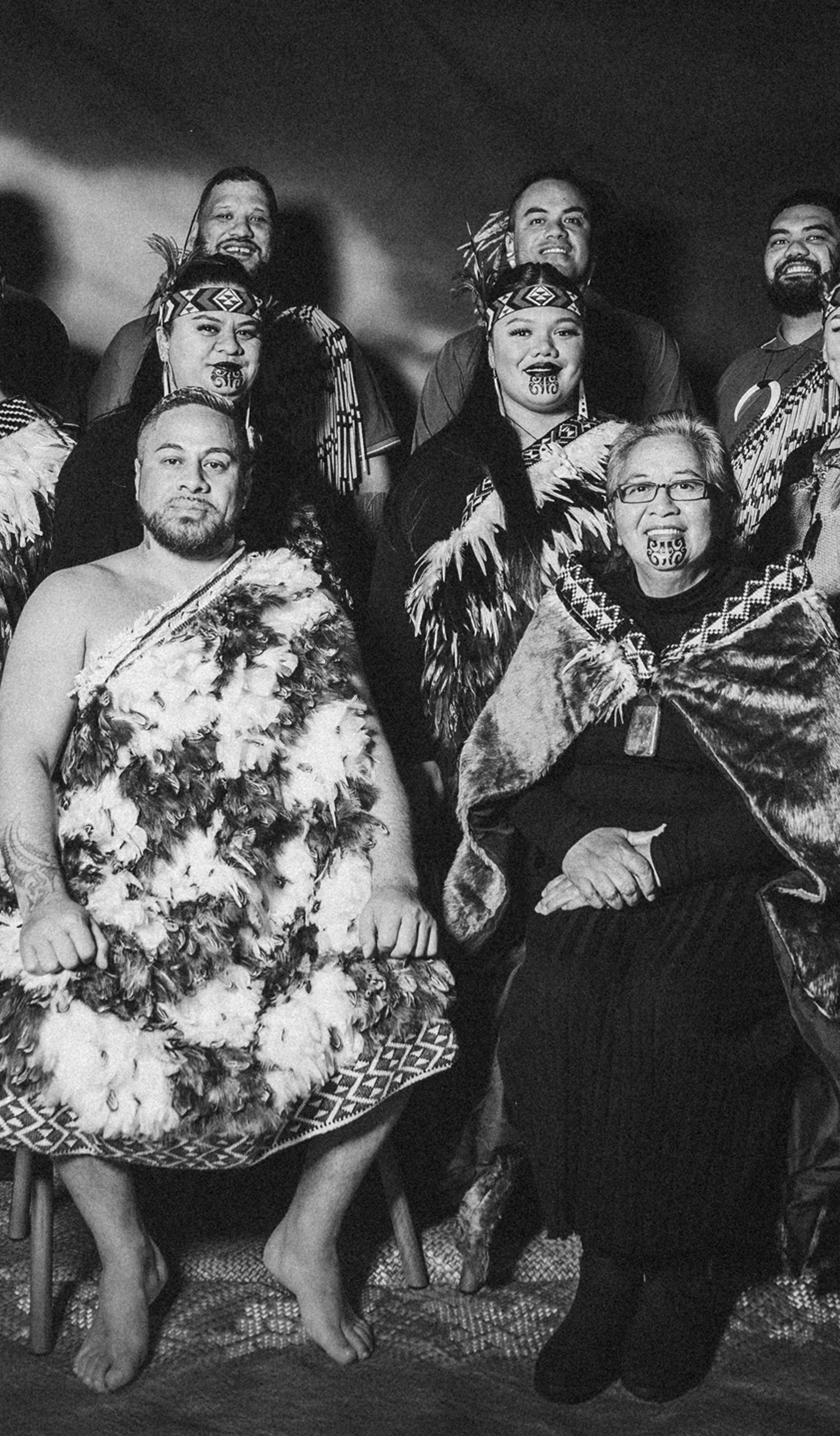 A black and white group portrait of the kapa haka group, Te Raranga Whānui. Seated at the front are Laurie Sarich, Neta Sarich. Behind them are Casey Fenton, Moana McLeod, Ashley Simon, Marei Peters, Hope Harris, Tiana Tiakiwai. At the back are Conway McLeod, Rata McGregor Jnr, Josh Simon, Royal Kingi Pita.