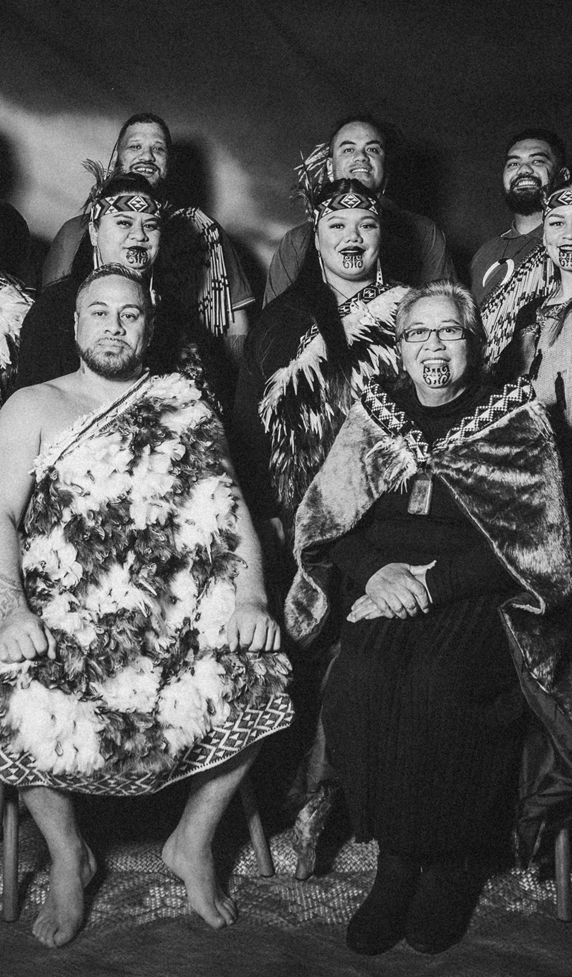 A black and white group portrait of the kapa haka group, Te Raranga Whānui. Seated at the front are Laurie Sarich, Neta Sarich. Behind them are Casey Fenton, Moana McLeod, Ashley Simon, Marei Peters, Hope Harris, Tiana Tiakiwai. At the back are Conway McLeod, Rata McGregor Jnr, Josh Simon, Royal Kingi Pita.