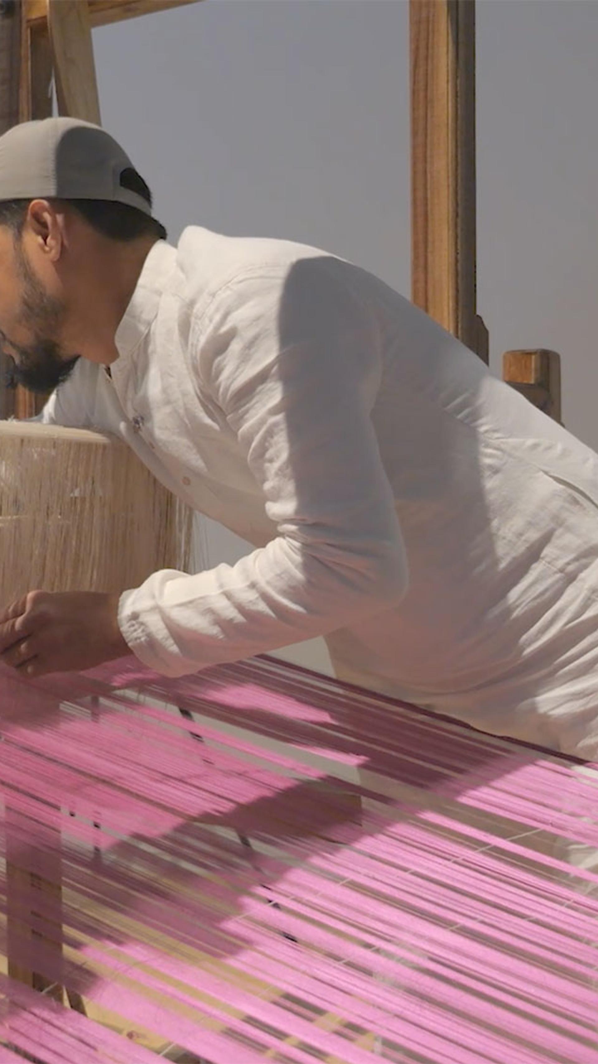 A figure using a loom with pink and beige threads