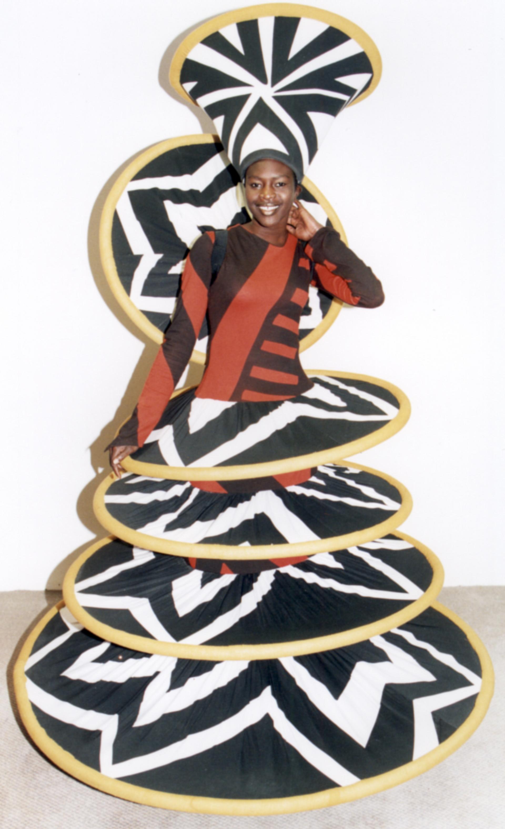 A woman dress in a brown, orange, yellow and black costume that has layered discs from the waist down.
