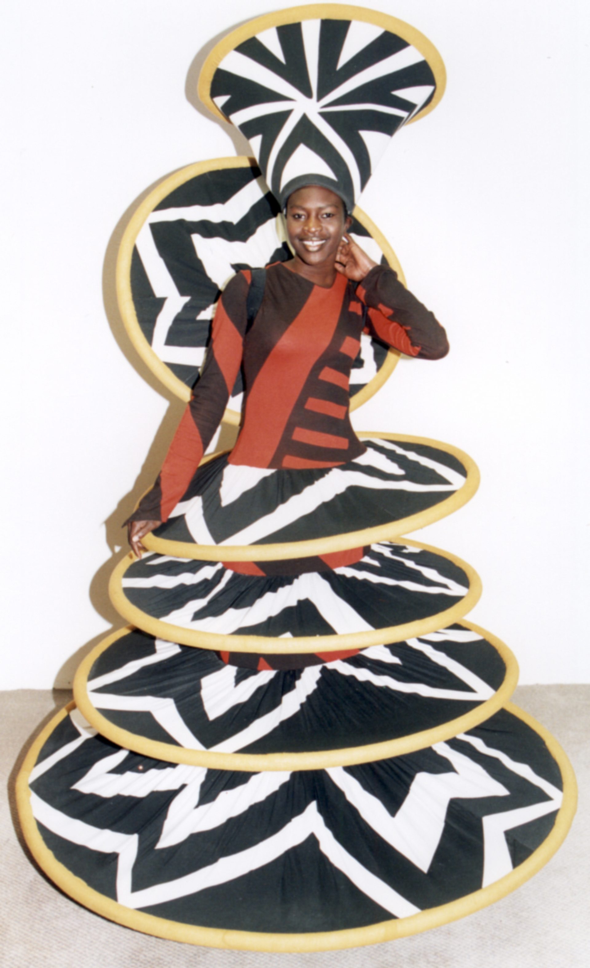 A woman dress in a brown, orange, yellow and black costume that has layered discs from the waist down.