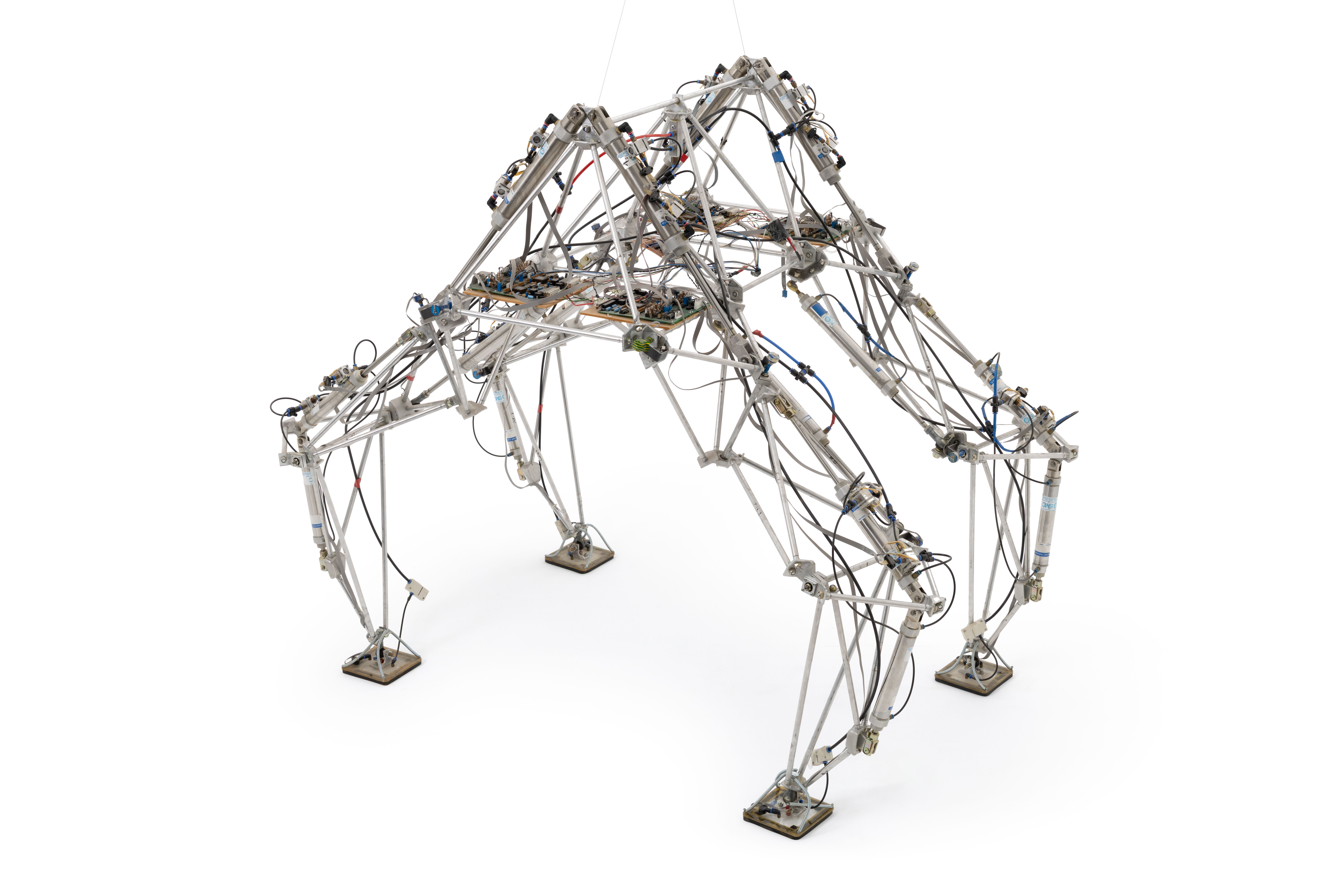 Large prototype robot with angular body and four legs constructed from lengths of aluminium tubing and electronic wiring. Each leg features a suction plate or pad at the end to provide greater steadiness on different surfaces. The legs are articulated and allow the robot to walkand move.