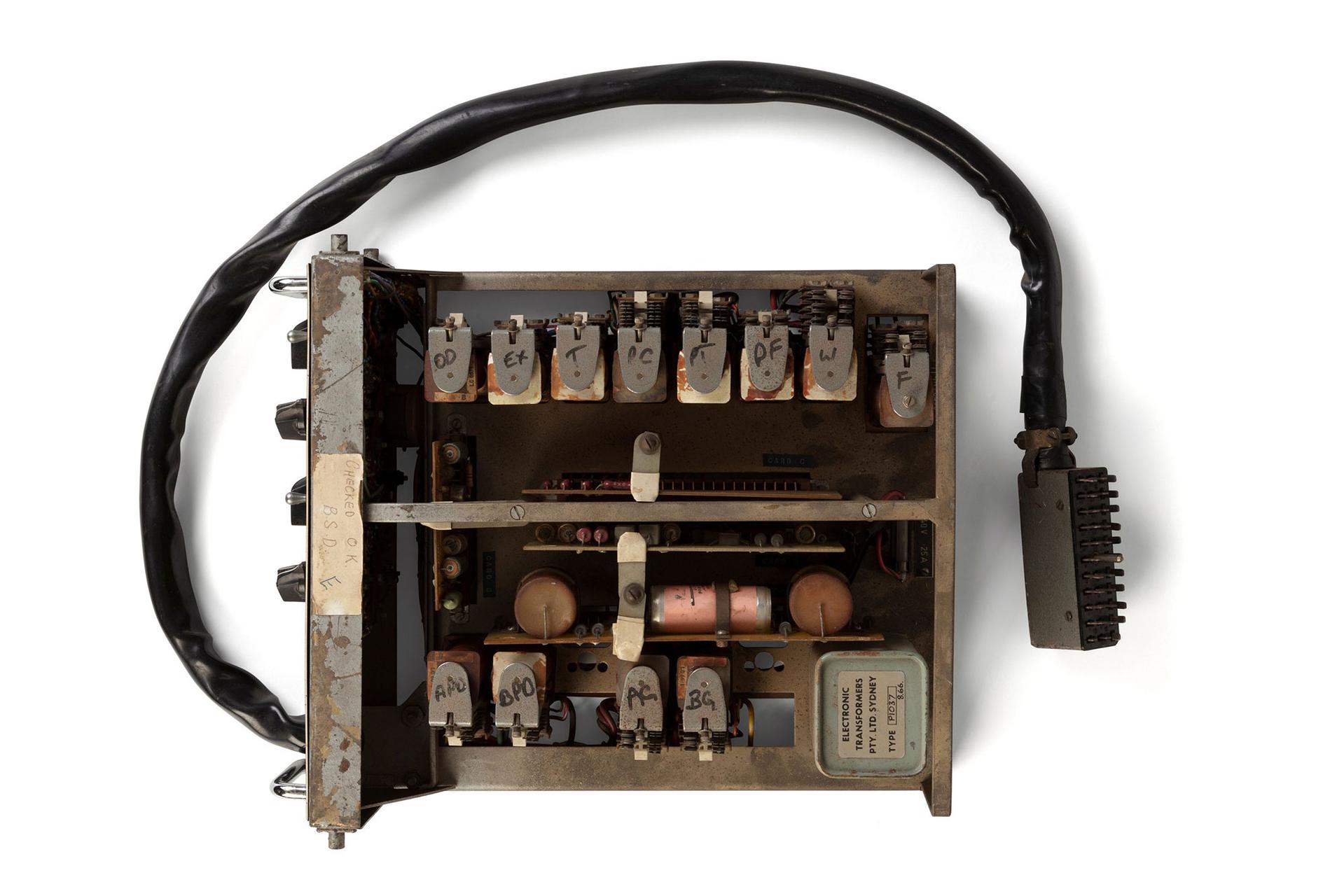 The PX-2 is a control housed in a metal rack designed to be secured in a traffic control box that you see by the side of the road near traffic control lights. It has relay-logic electronic circuits that control the duration and sequence of light signal events that occur at a pedestrian crossing. There is a black painted metal plate and dials at the front of the unit that permit the adjustment of times dependent upon the size of the intersection at which it is to be installed. There is a large multi-core cable which runs from the unit to a connector.