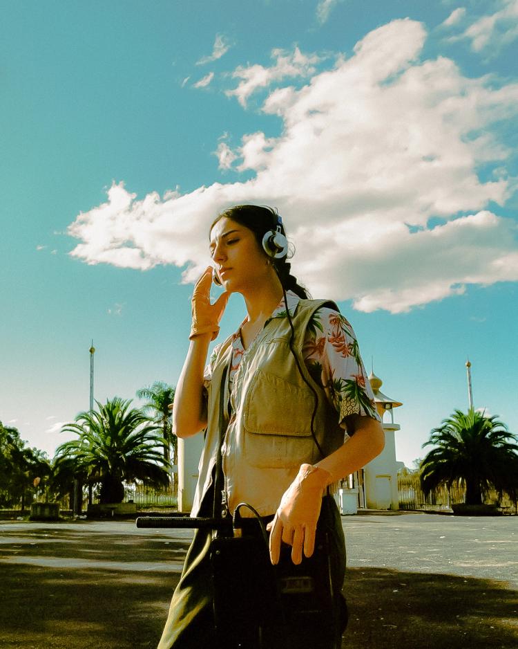A young woman stands alone in an empty parking lot with her headphones on, listening to sounds.