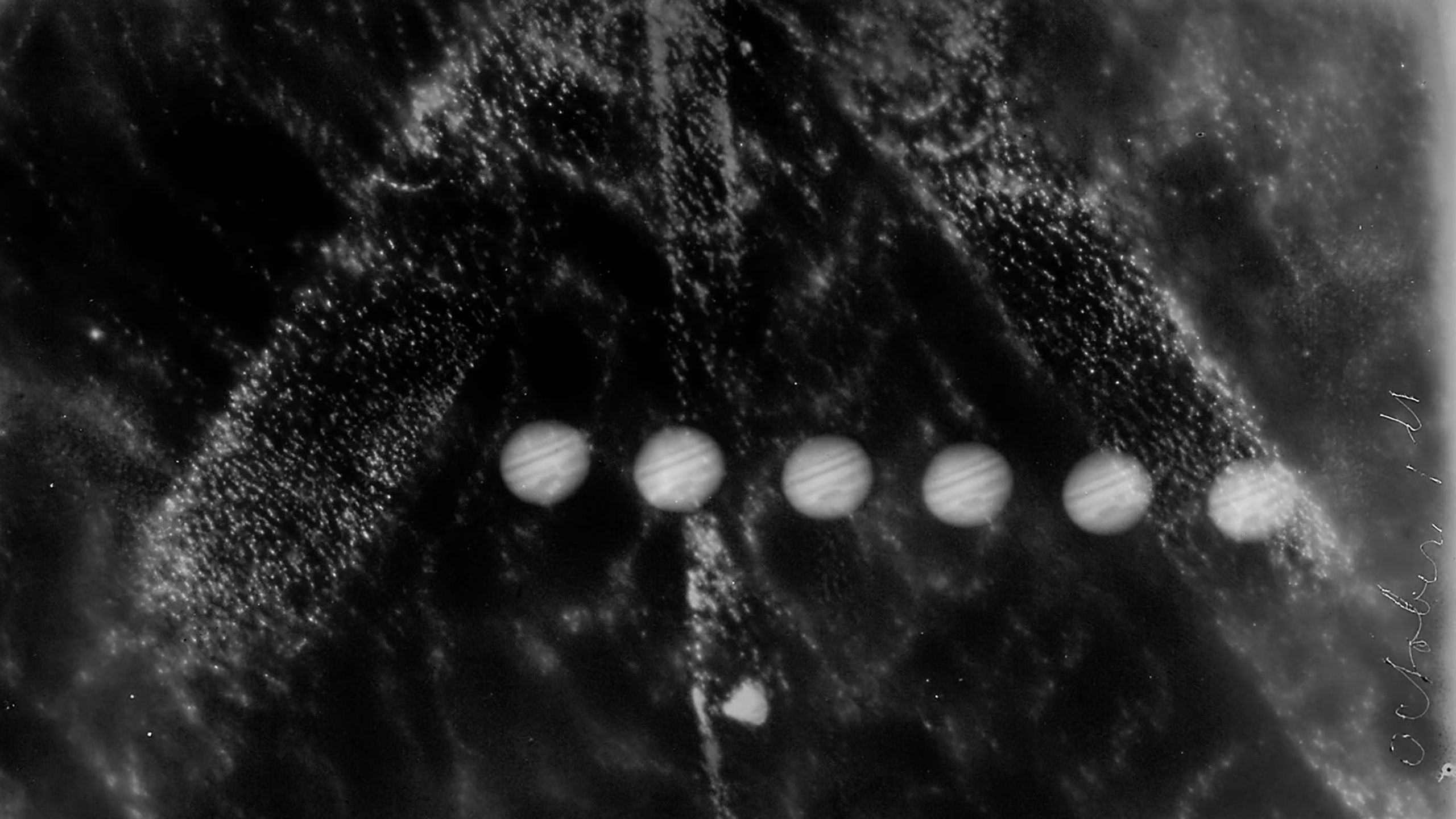 A rectangular black and white silver gelatin glass plate positive showing six images of Jupiter. The original storage envelope accompanies the glass plate.