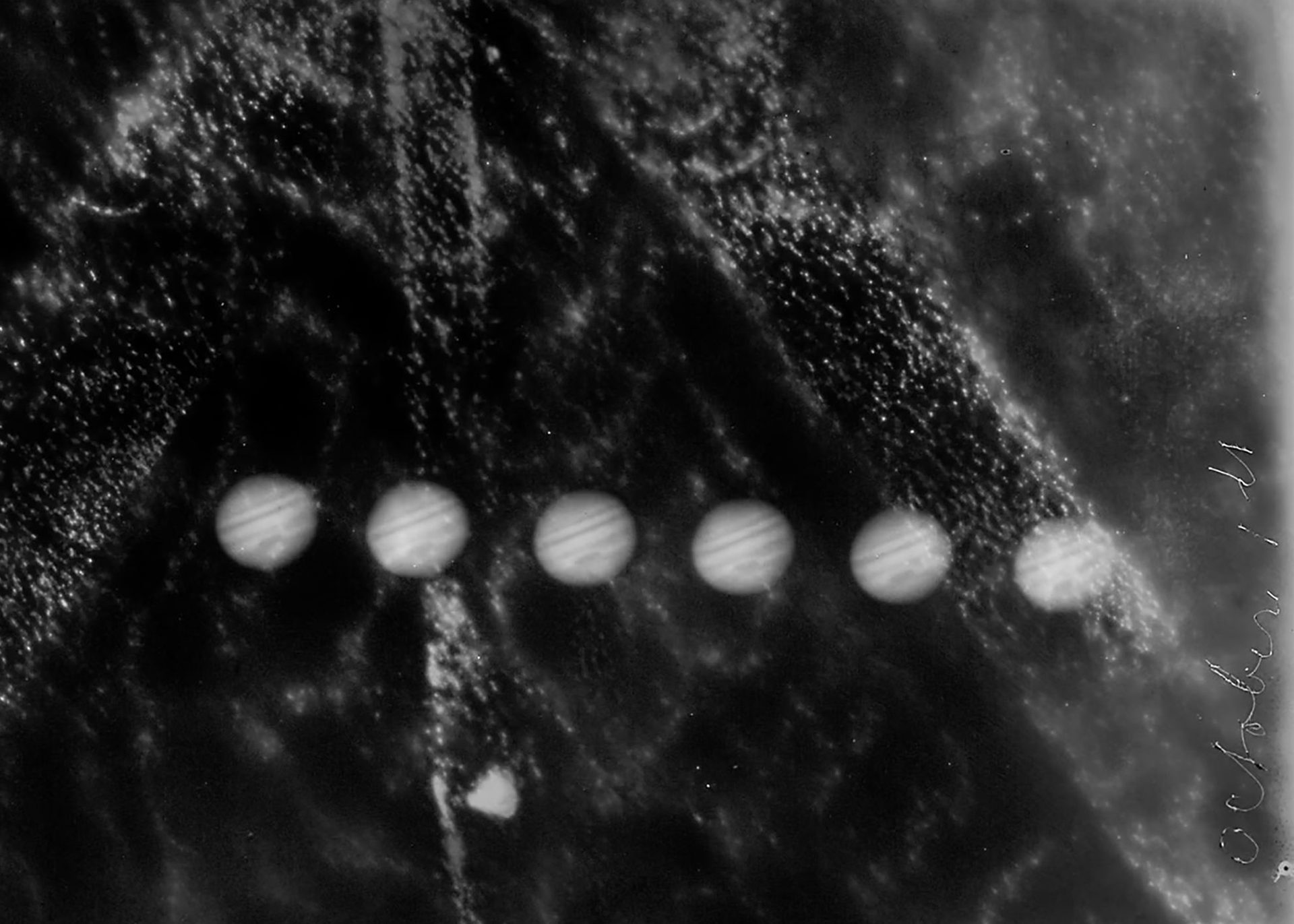 A rectangular black and white silver gelatin glass plate positive showing six images of Jupiter. The original storage envelope accompanies the glass plate.