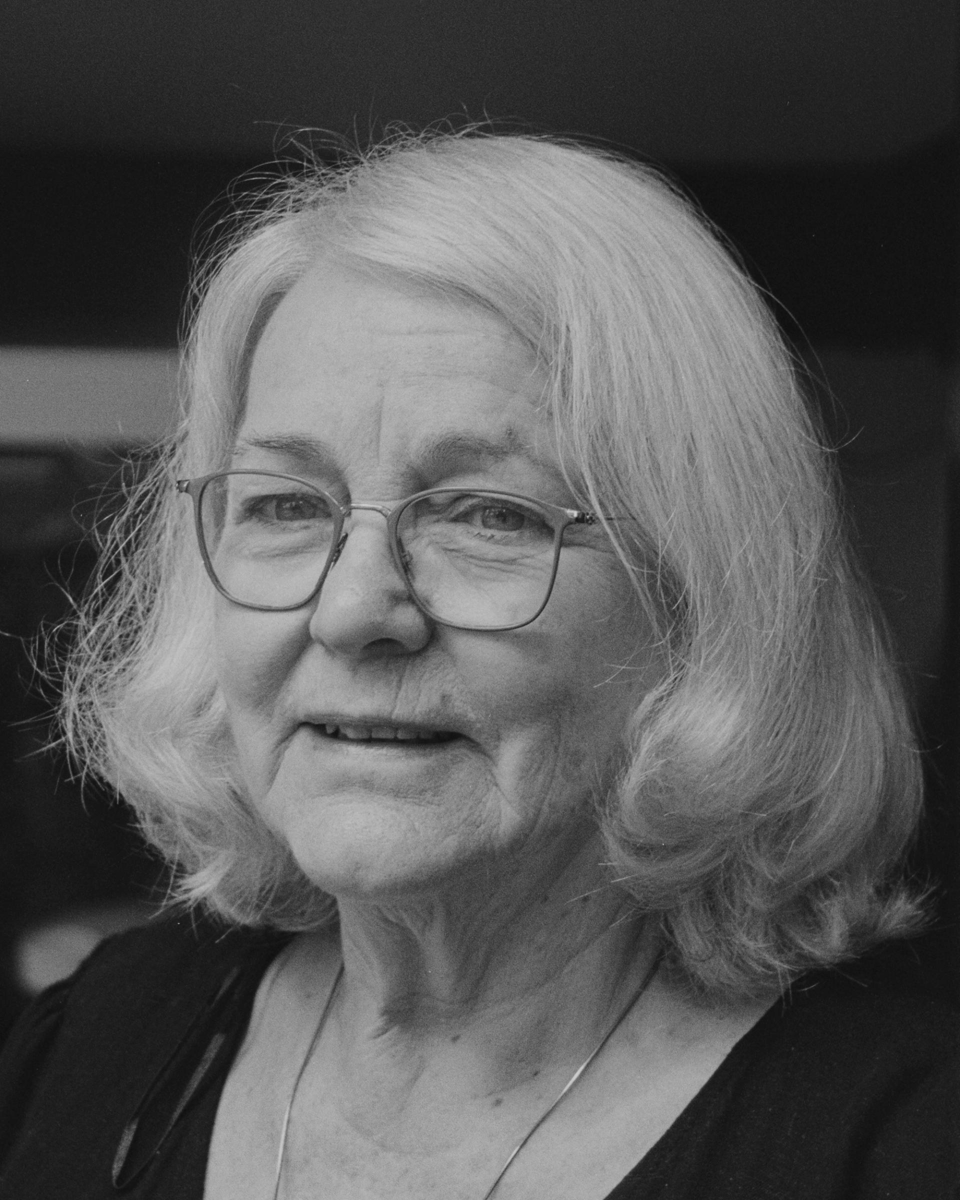 Close up black and white portrait of a woman (Barbara Stokes) with short gray hair and glasses.