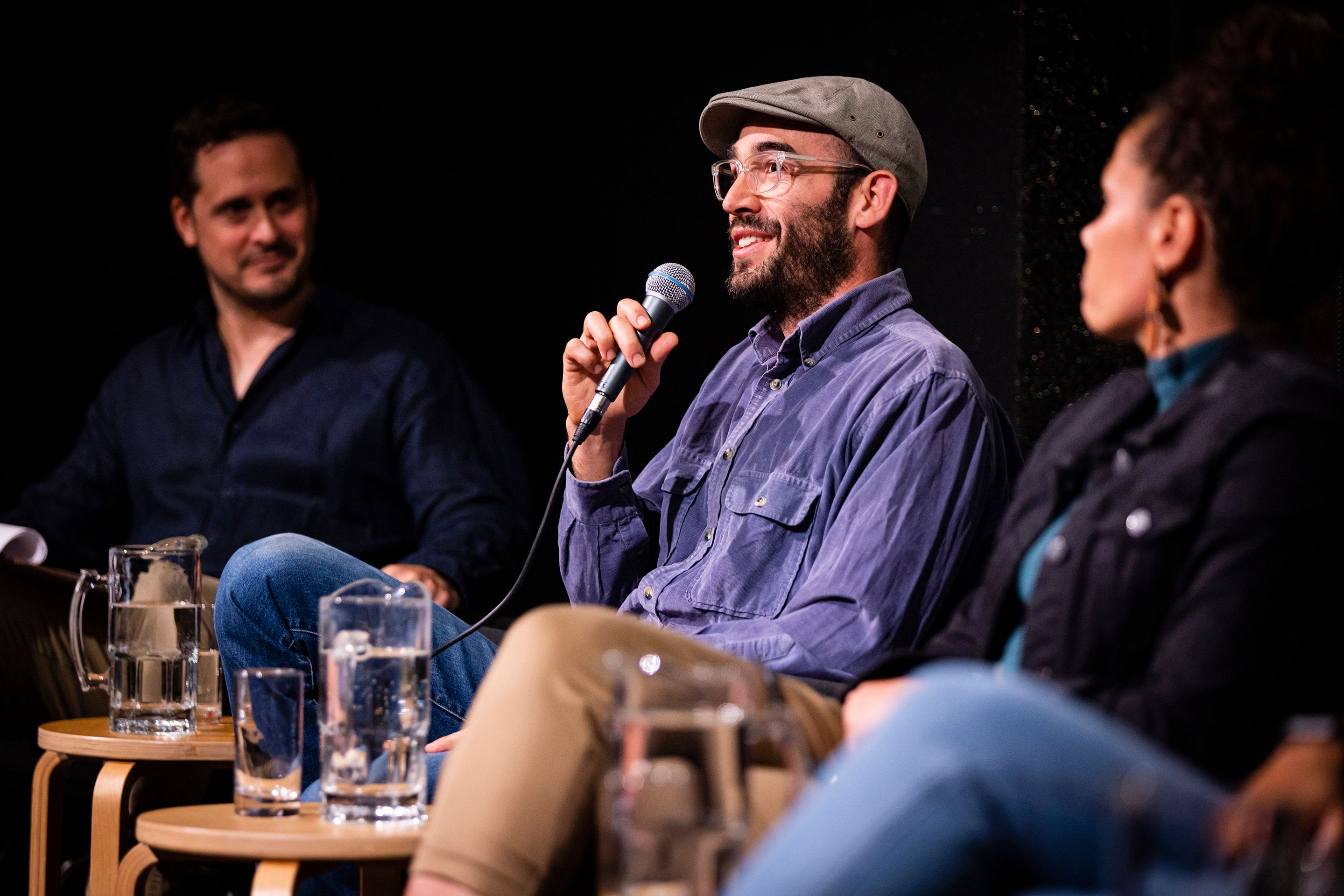 Three panelists, with the man wearing a hat in the middle talking on the microphone