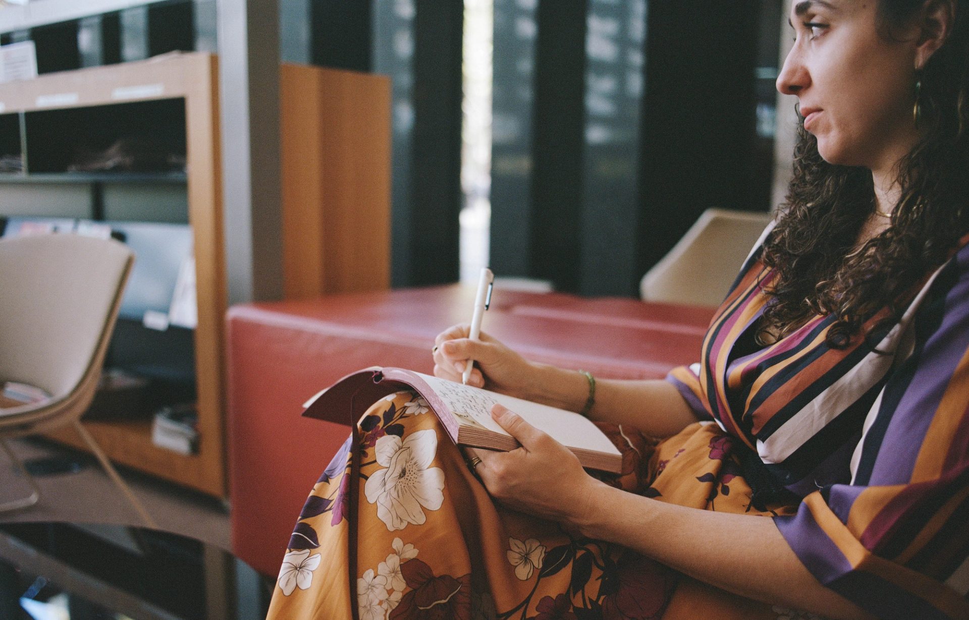 Person sitting with their left side to the camera, writing in a book.