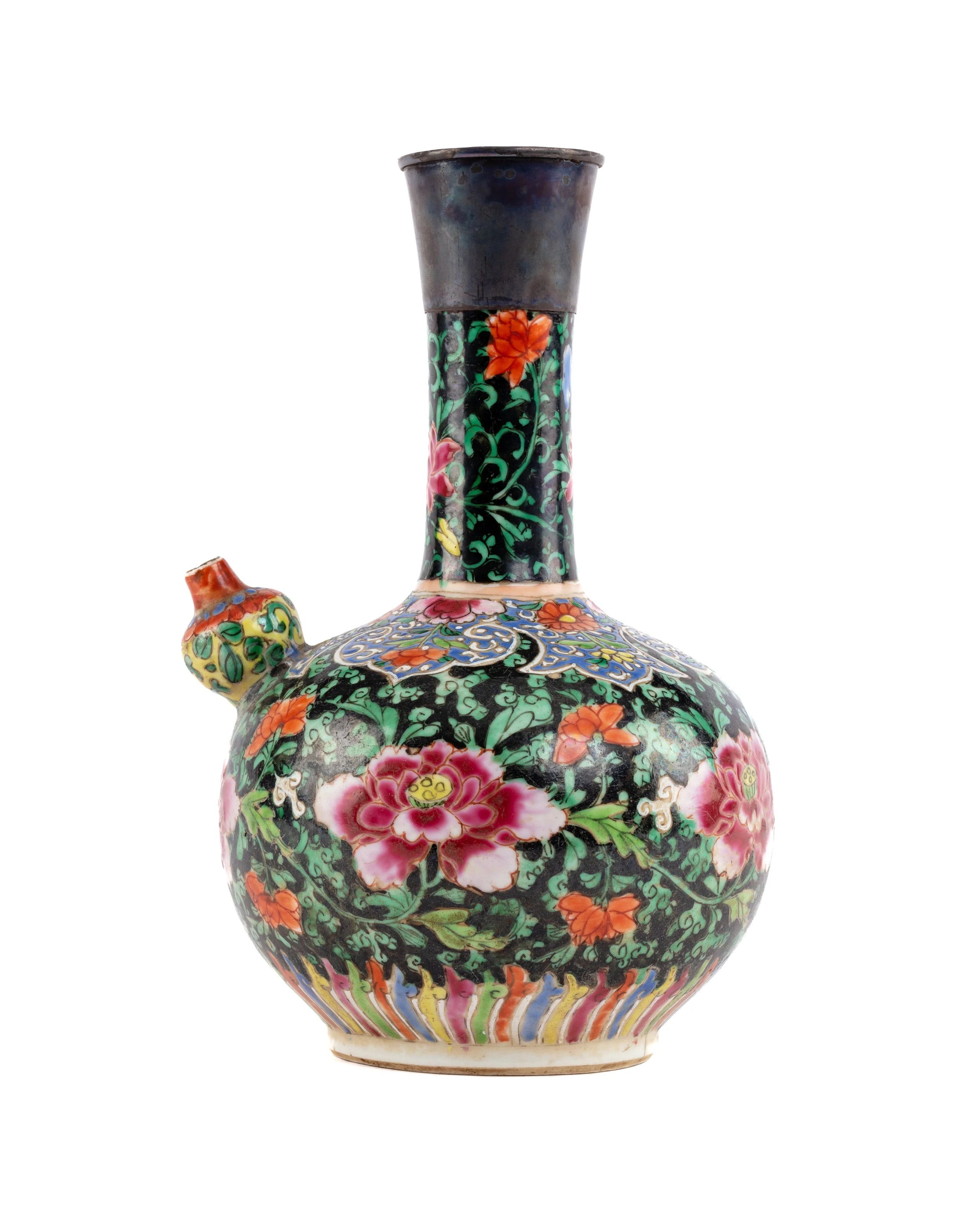 A porcelain wine vessel decorated with coloured flowers atop a green and black ground.