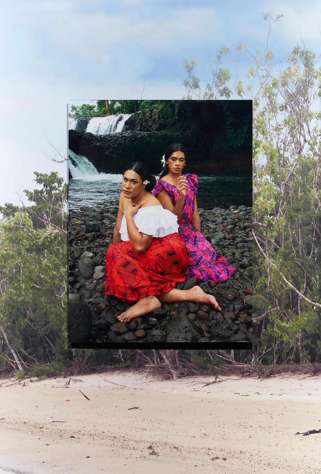 Image of two faʻafafine sitting on the rocky bank of a waterfall.