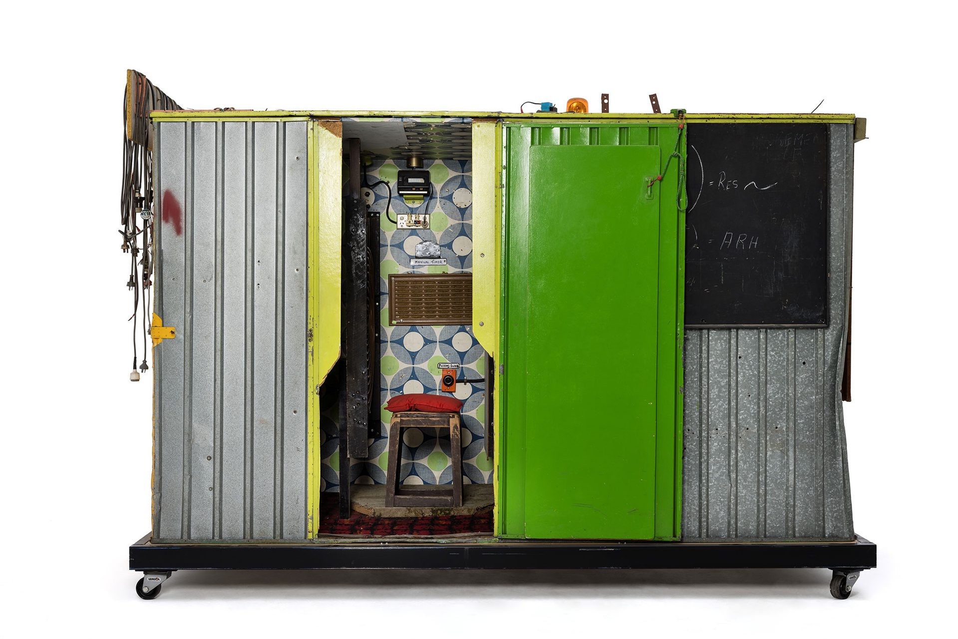 Green and yellow metal 'garden' shed containing elaborate electronic systems built into the interior. Inside the shed is a compartment which contains a seat where the user can sit and be suffused with radio waves produced by the electronic system.
