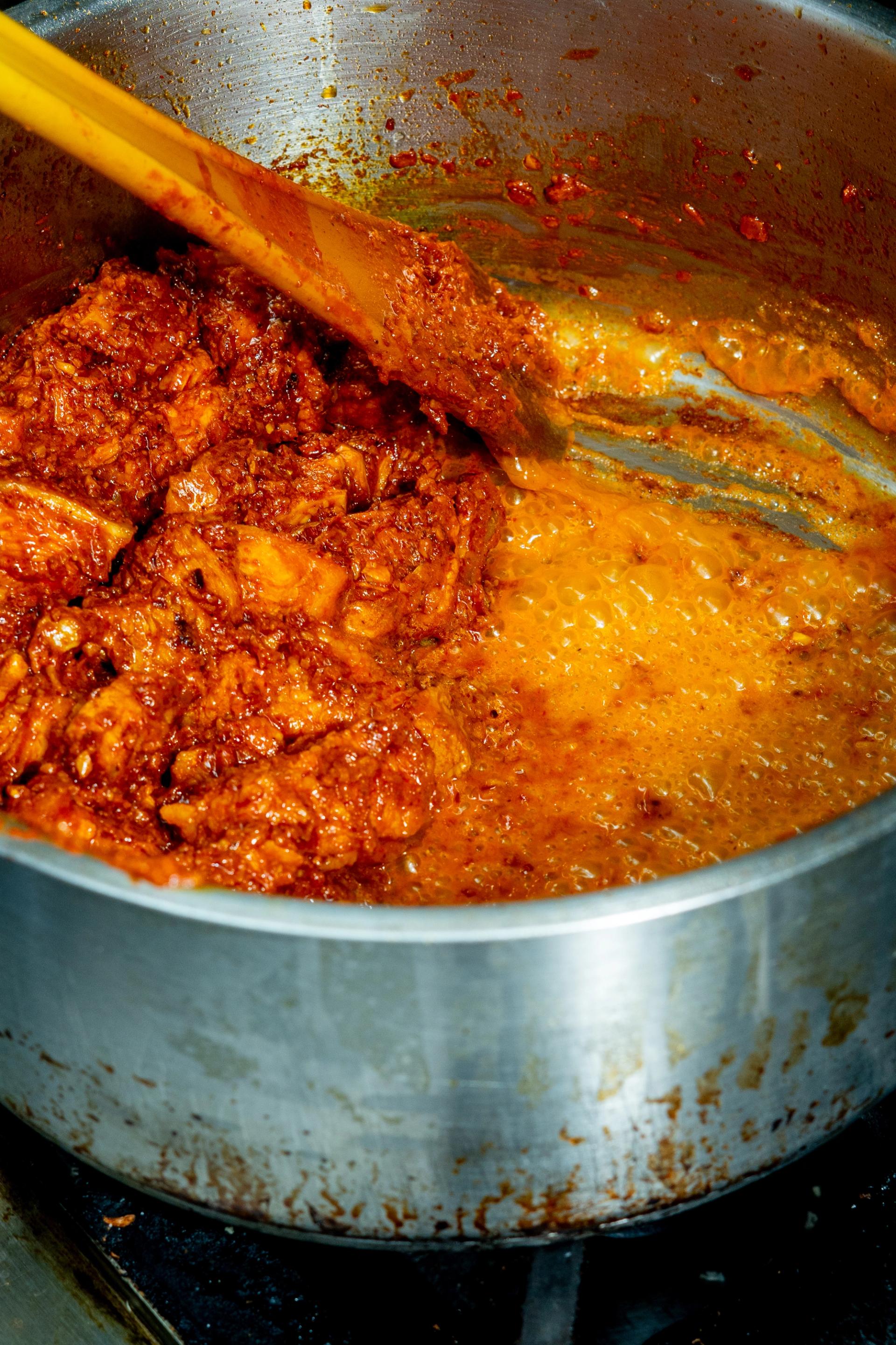 A large silver pot of orange and red coloured curry on a stove top.
