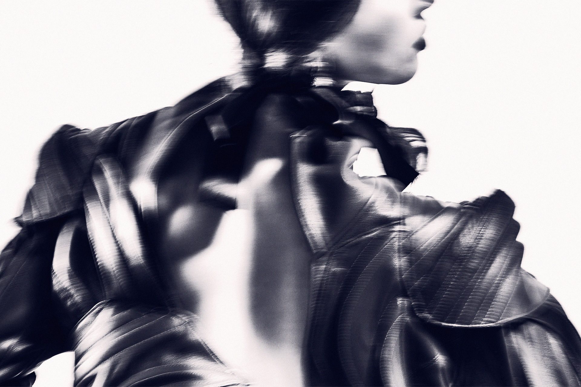 An abstract high contrast image of the back of a model, wearing a shiny leather jacket.