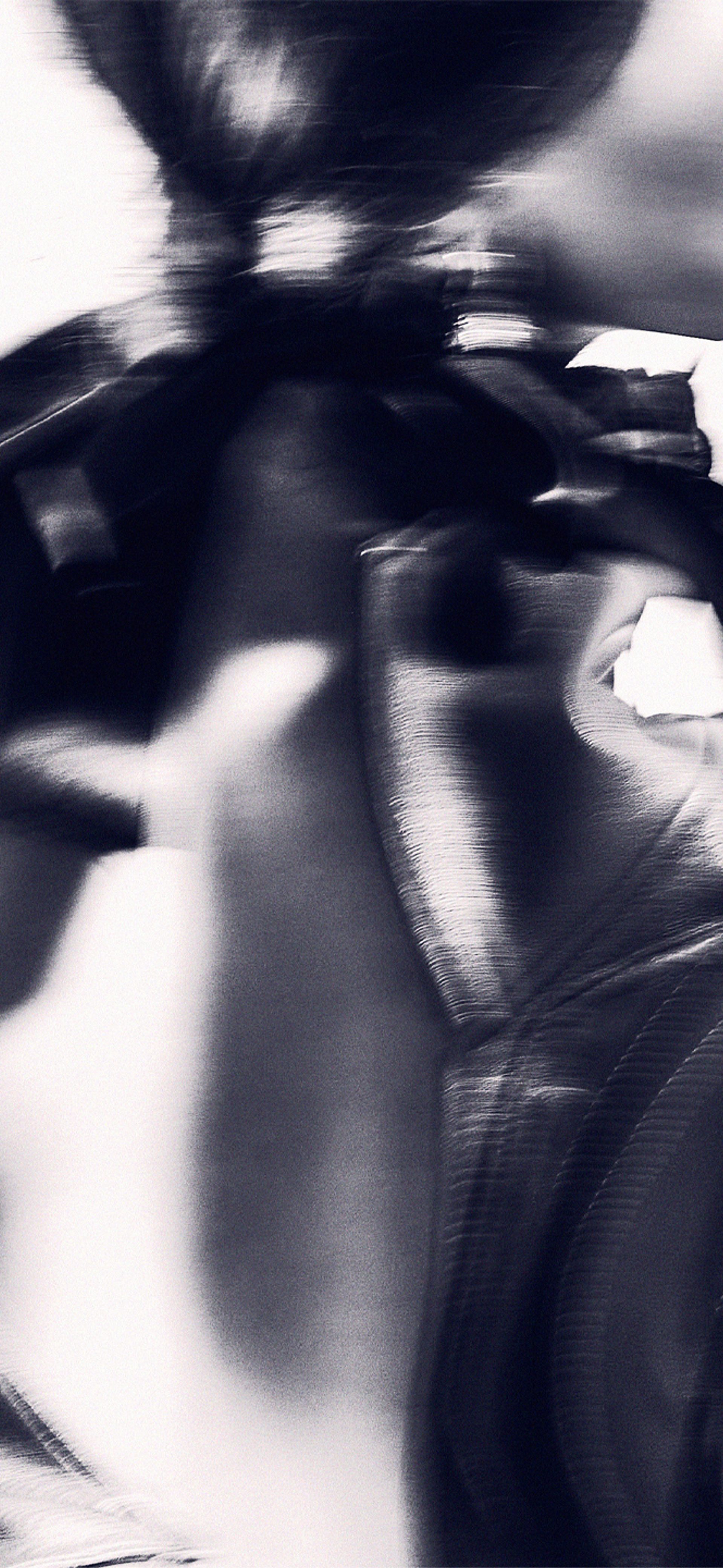 An abstract high contrast image of the back of a model, wearing a shiny leather jacket.