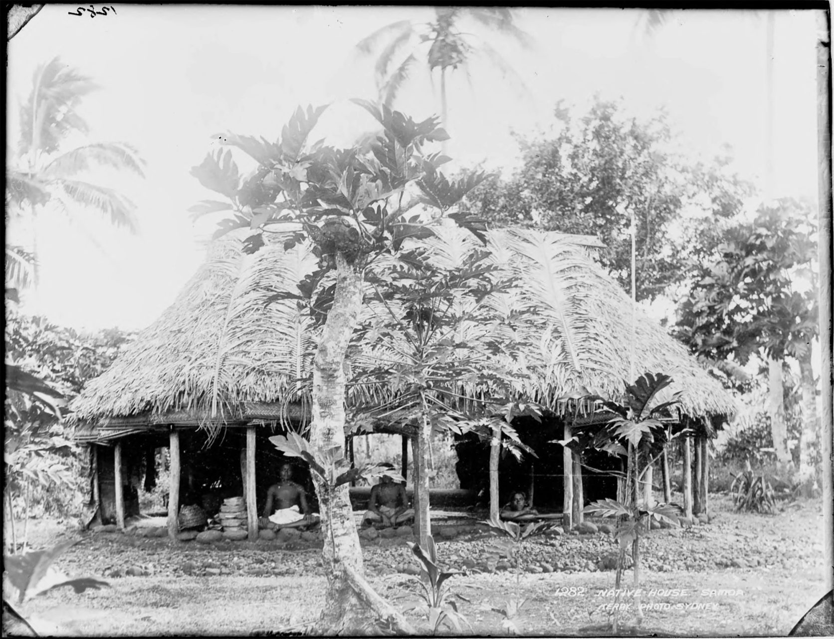Men sitting inside a roundhouse with a thatched roof.