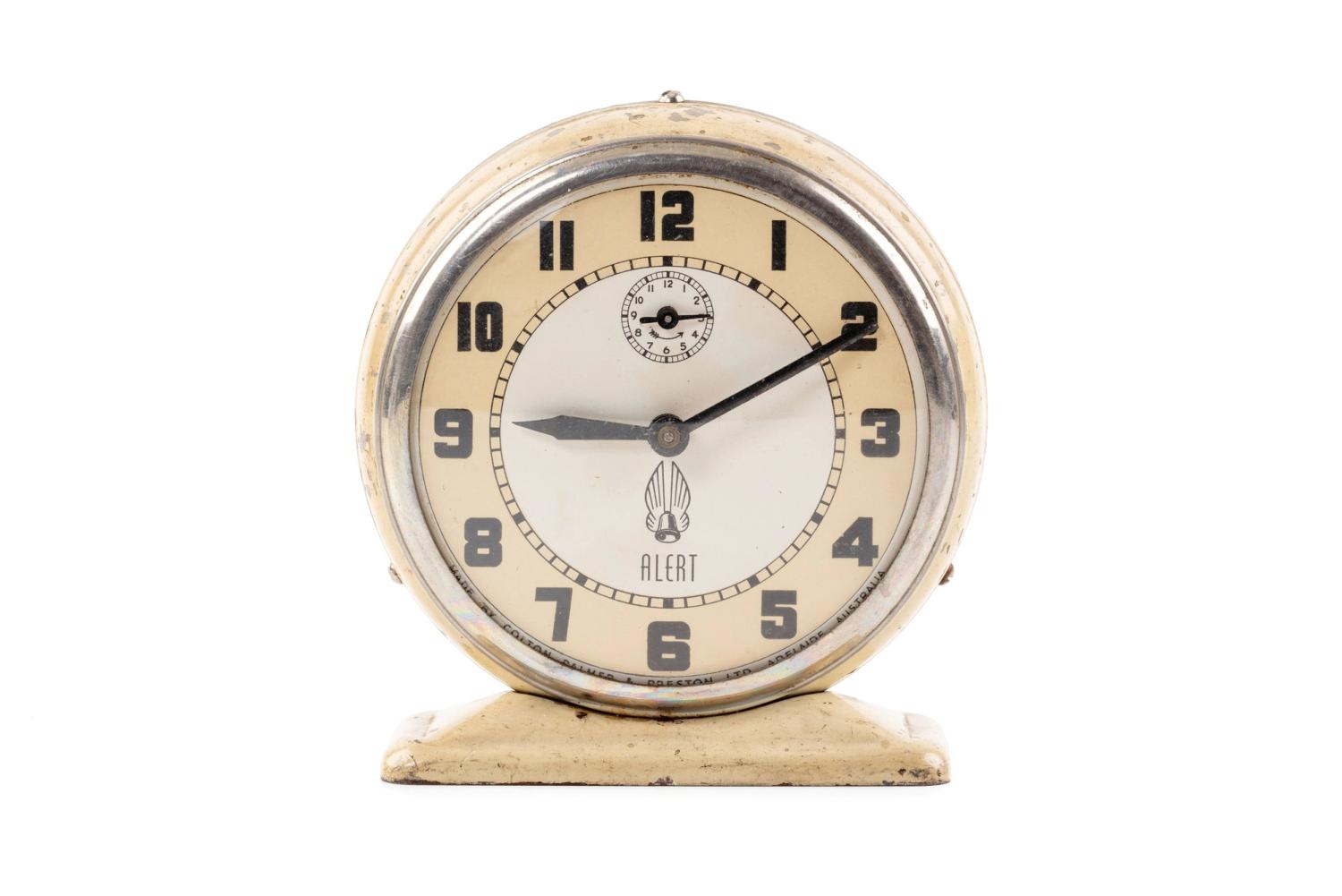 A cream, white and silver alarm clock with a circular face, on a white background