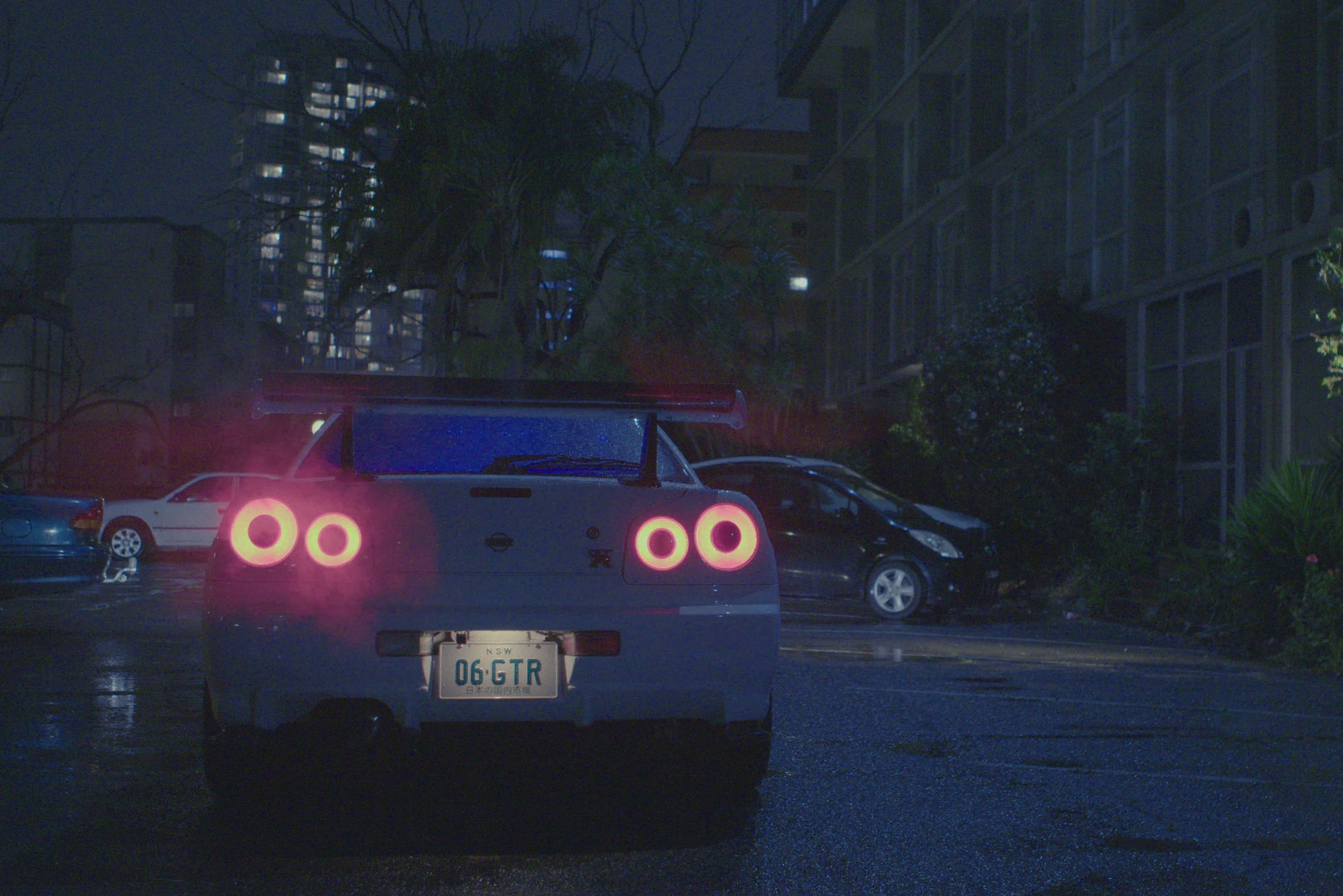 A still image of a car driving down a city street at night.