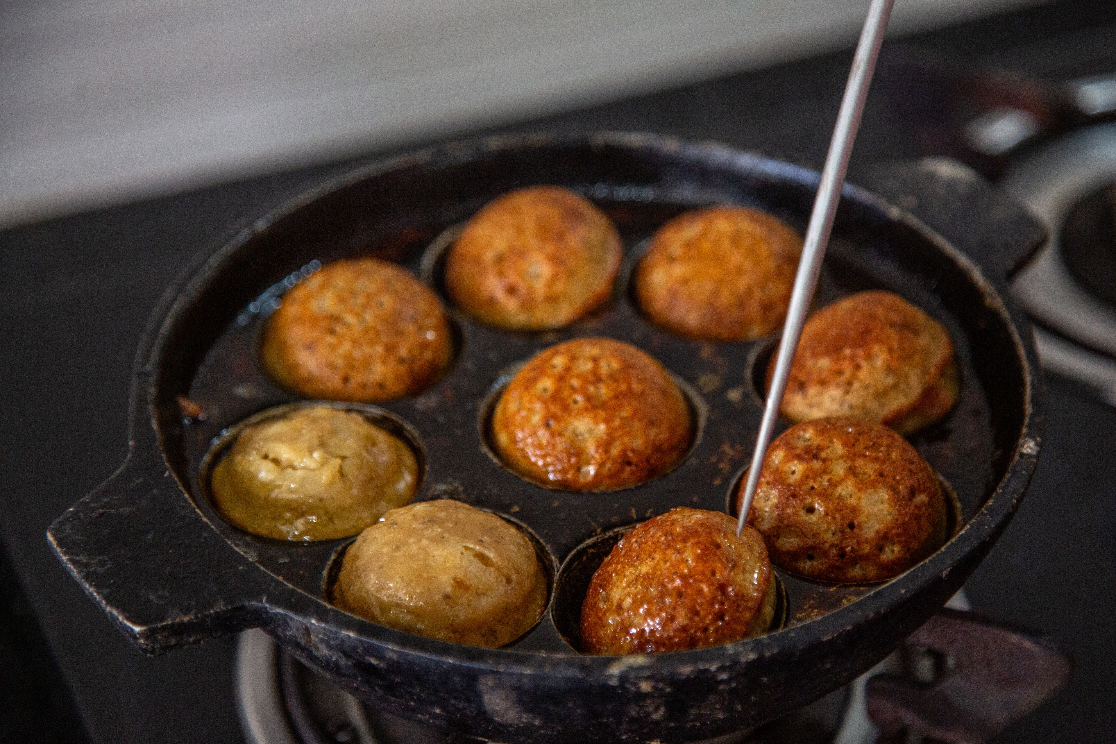 A paniyaram pan with cooked paniyaram. A silver skewer pokes at one of them.