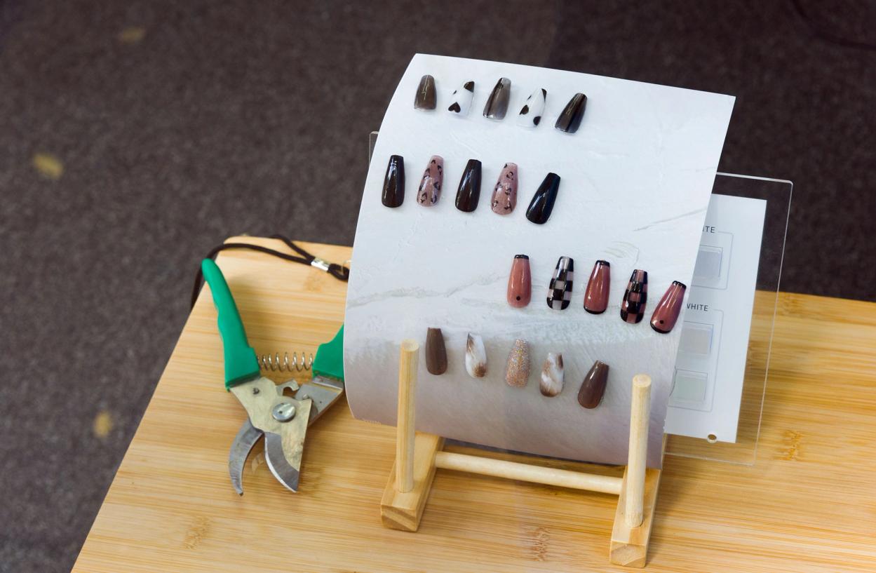 False nails in different patterns of pink, black, white and brown on a table with a pair of secateurs.