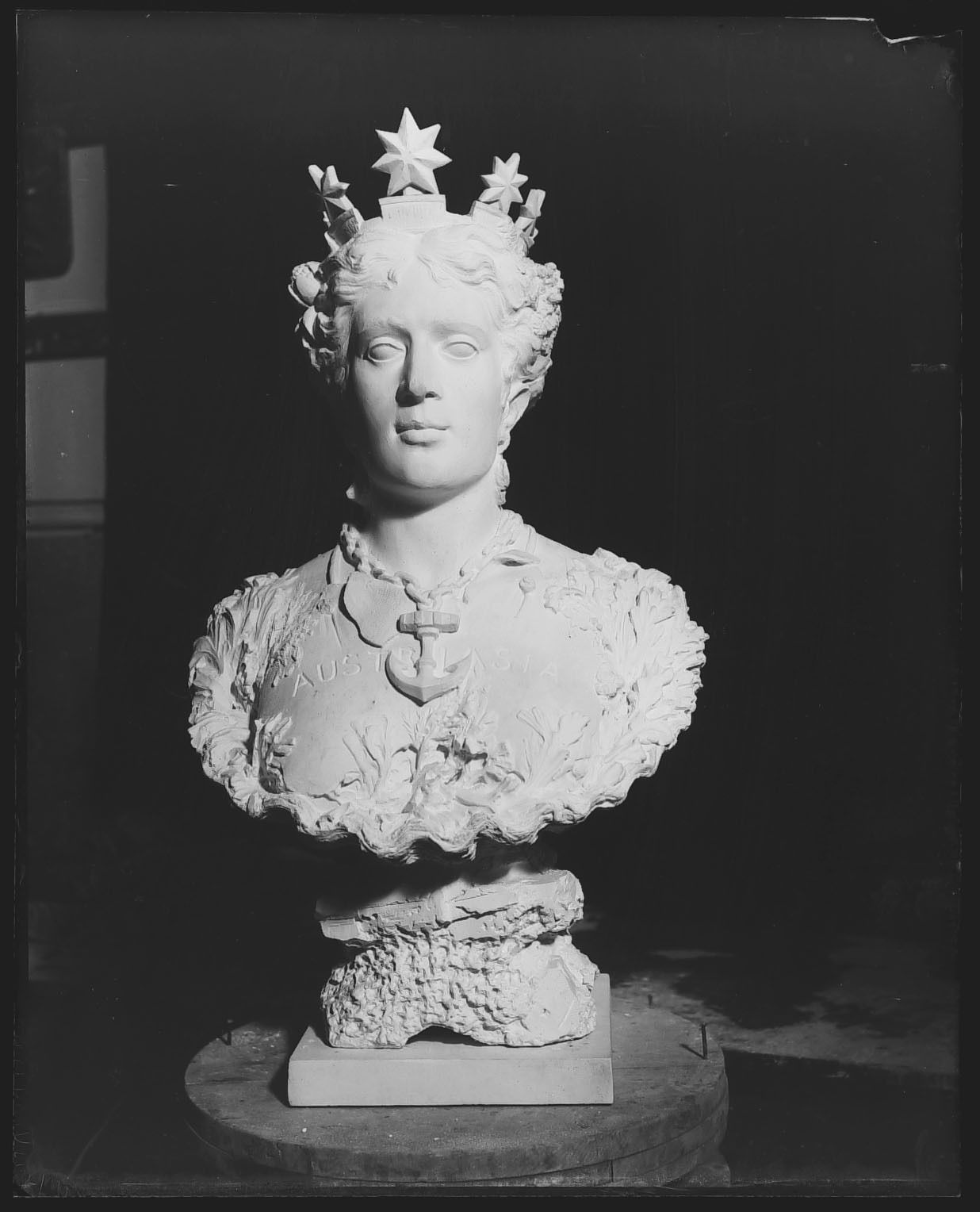 Glass plate negative of a plaster sculpture figure wearing a crown of stars and a necklace with a large anchor pendant. 'Australia' is carved into the plaster.