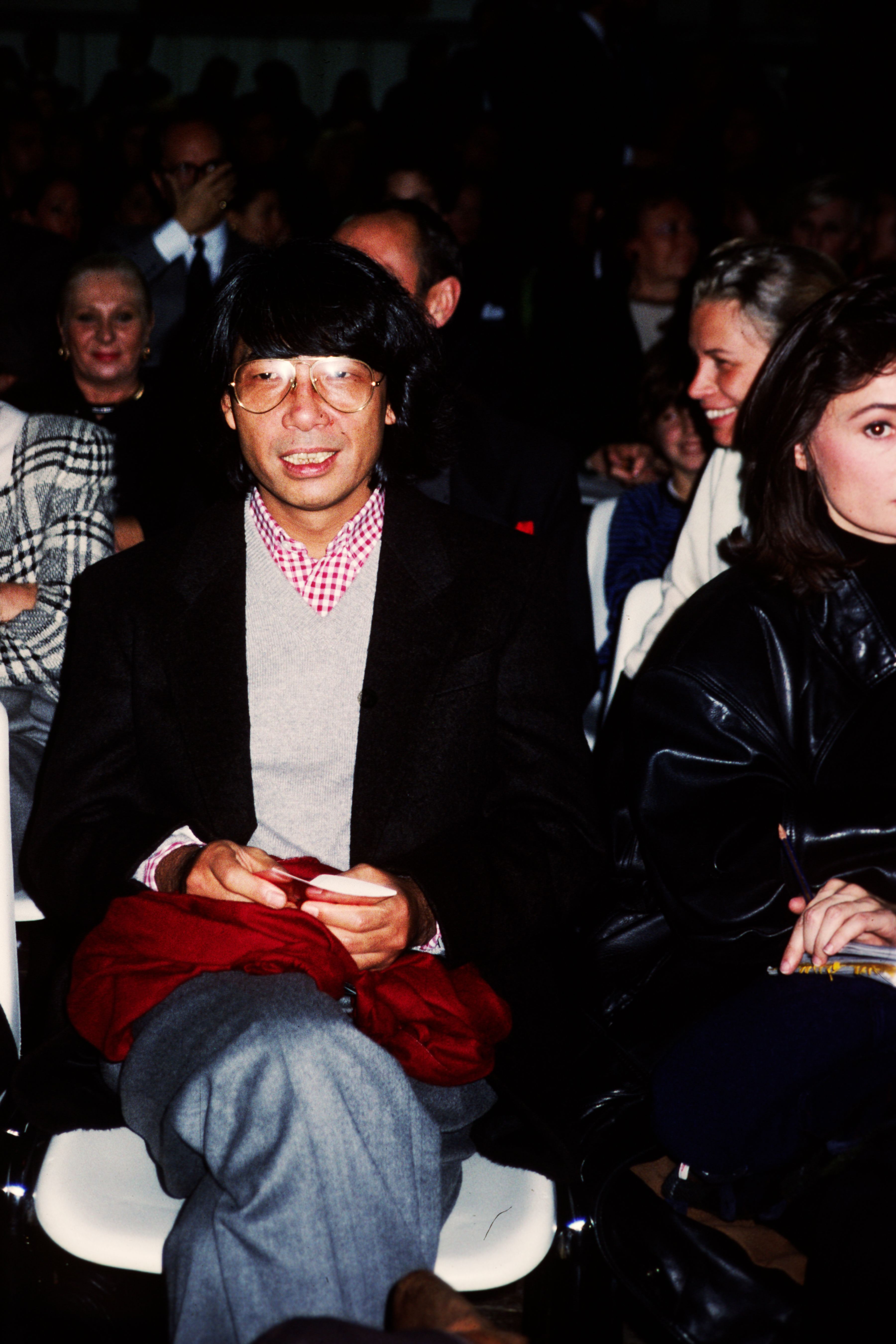Photograph of designer Kenzo Takada in Paris, 1989, sitting in a crowd for a runway show.