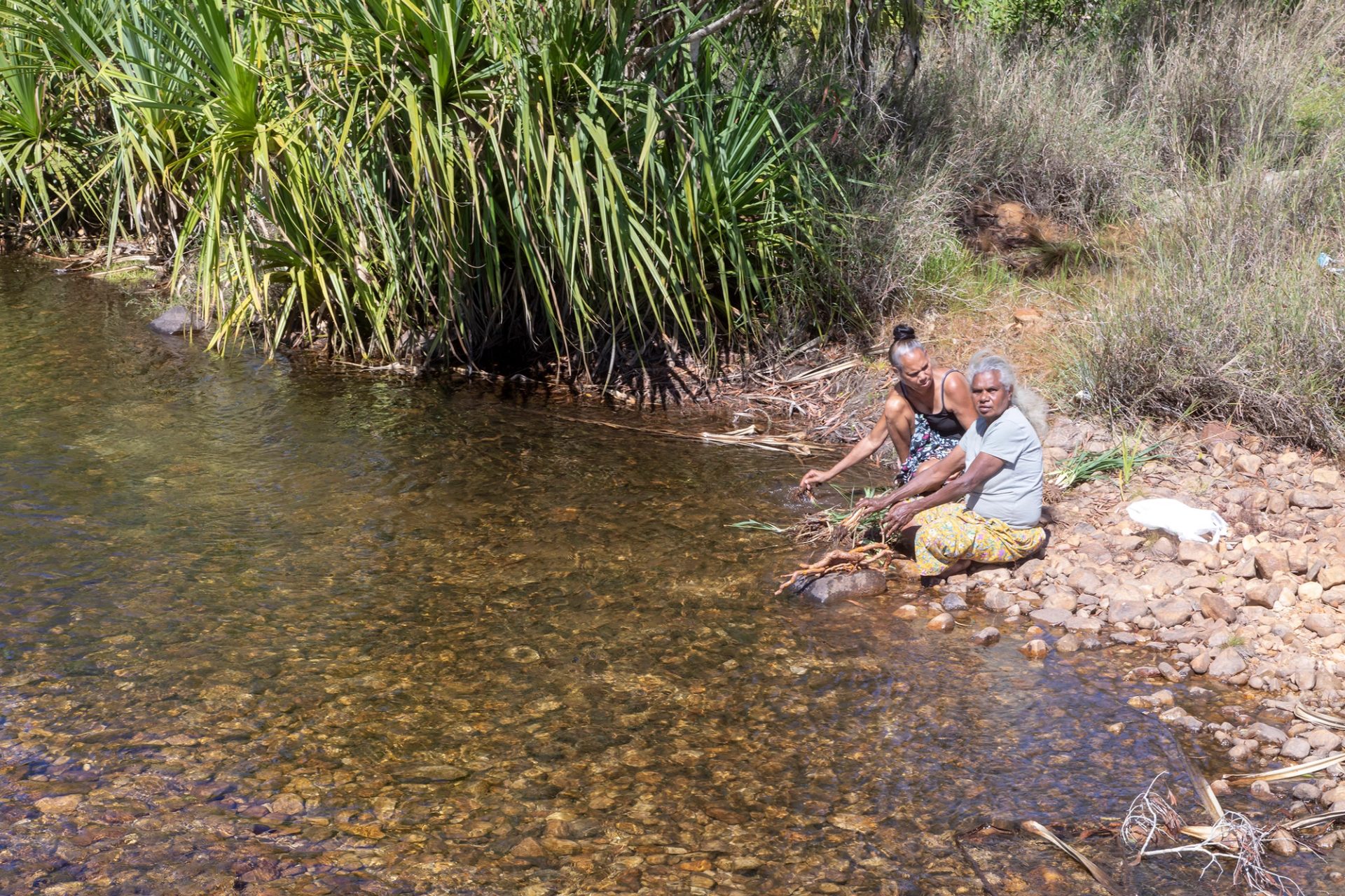 Two women sit on the rocky bed of a river.