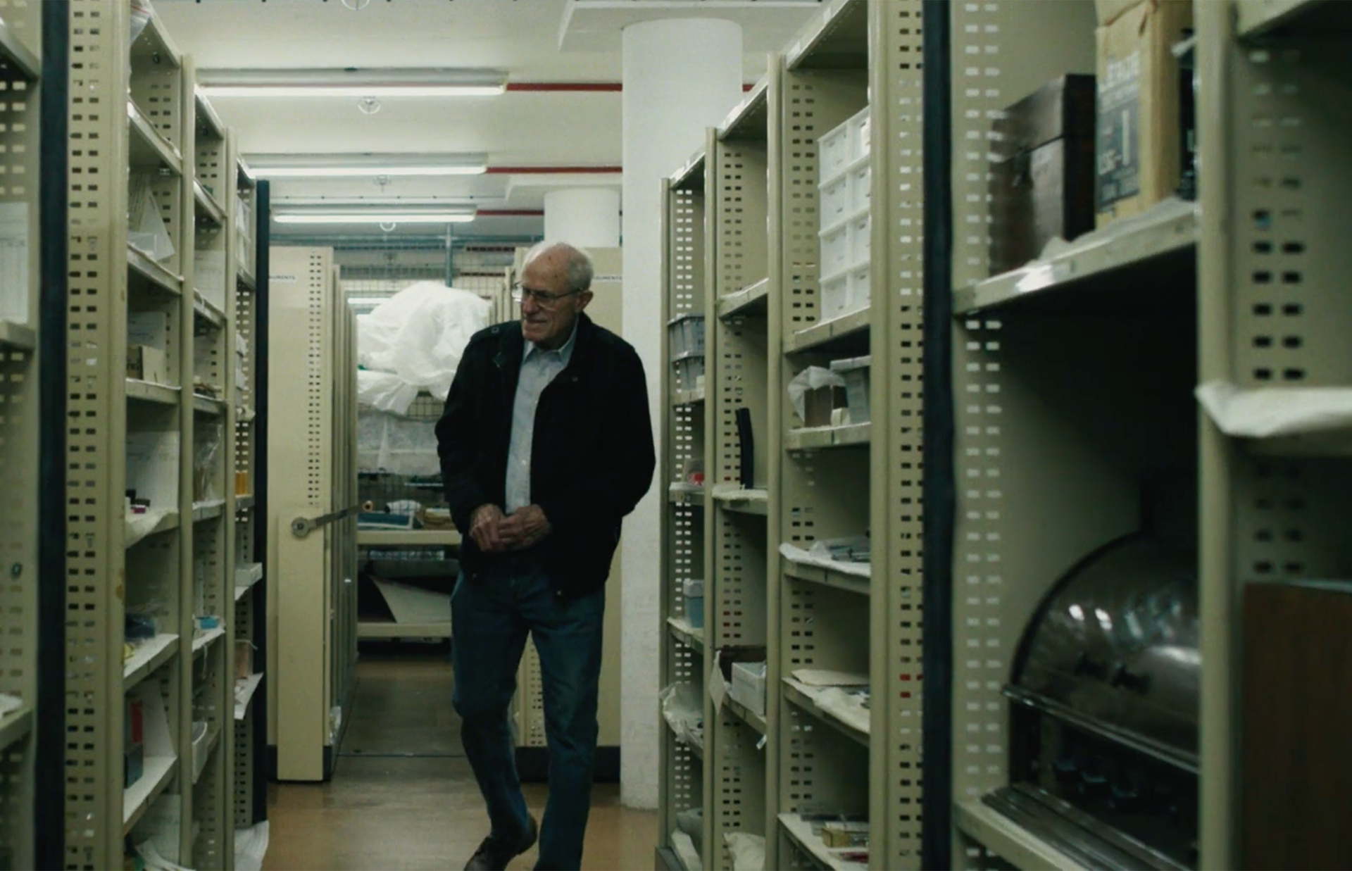 A figure walks through a corridor of shelves with typewriters on them