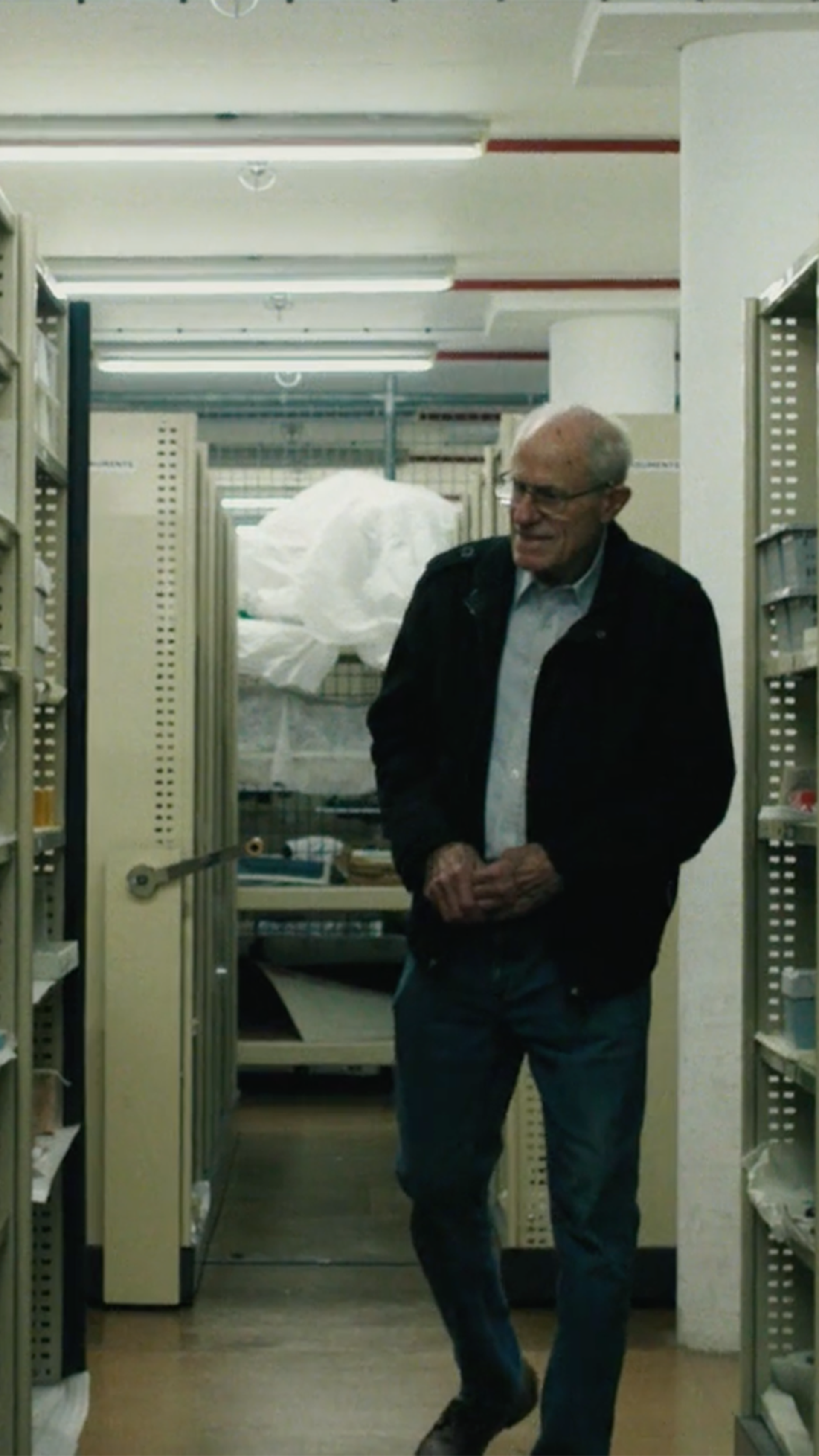 A figure walks through a corridor of shelves with typewriters on them